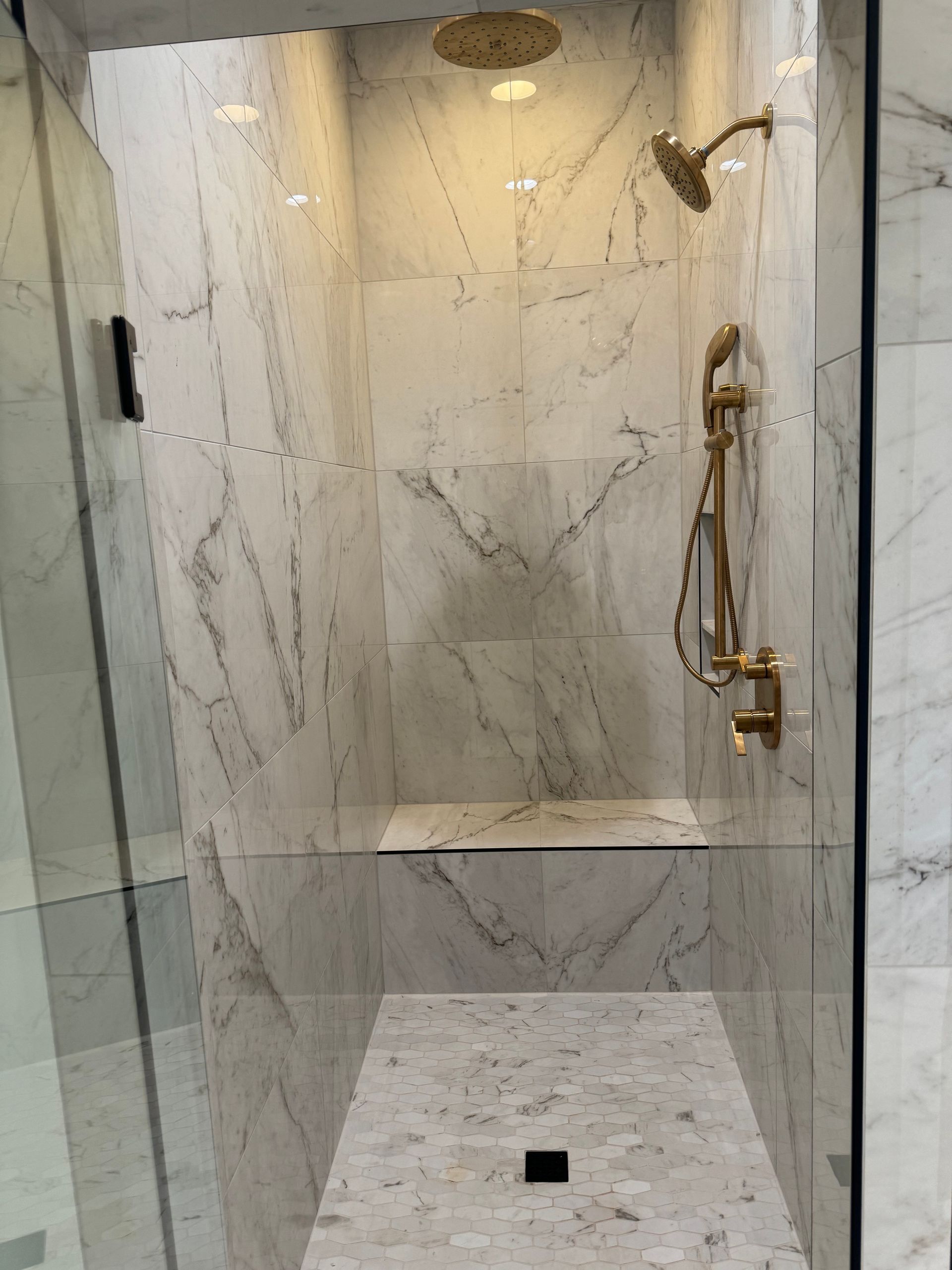 A walk in shower with marble walls and a gold shower head.