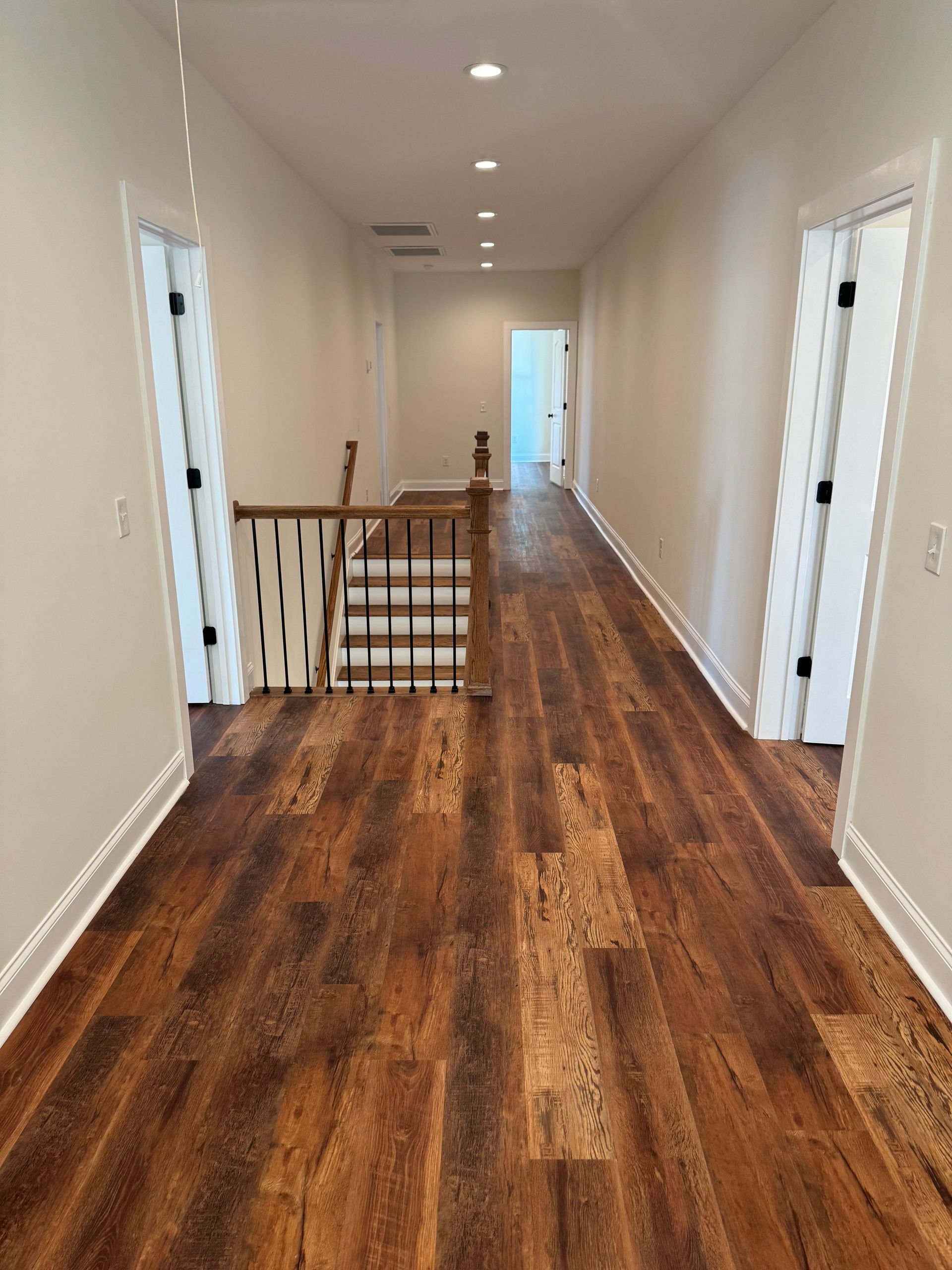 A long hallway with wooden floors and white walls leading to a staircase.