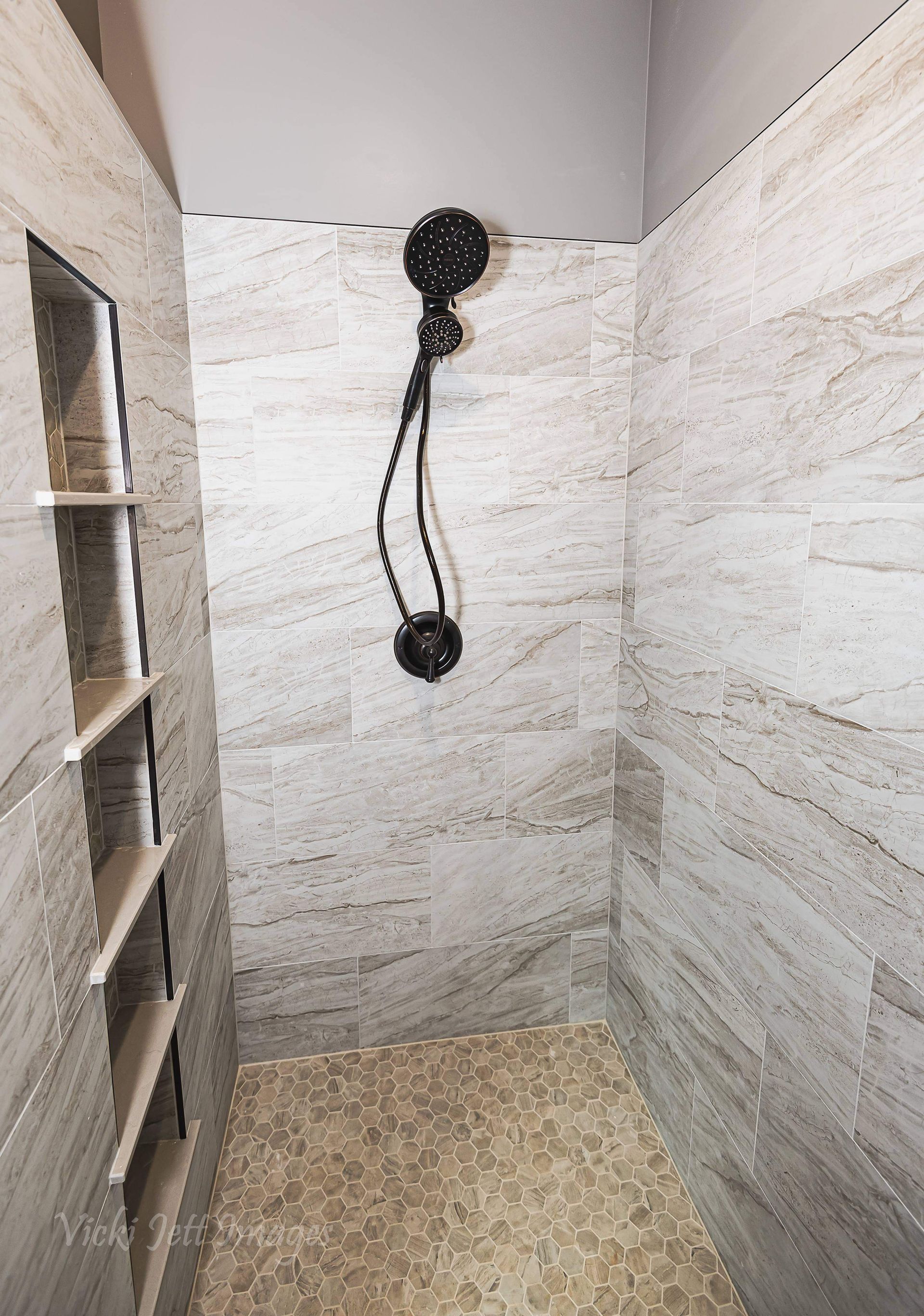 A shower with a black shower head hanging from the ceiling.
