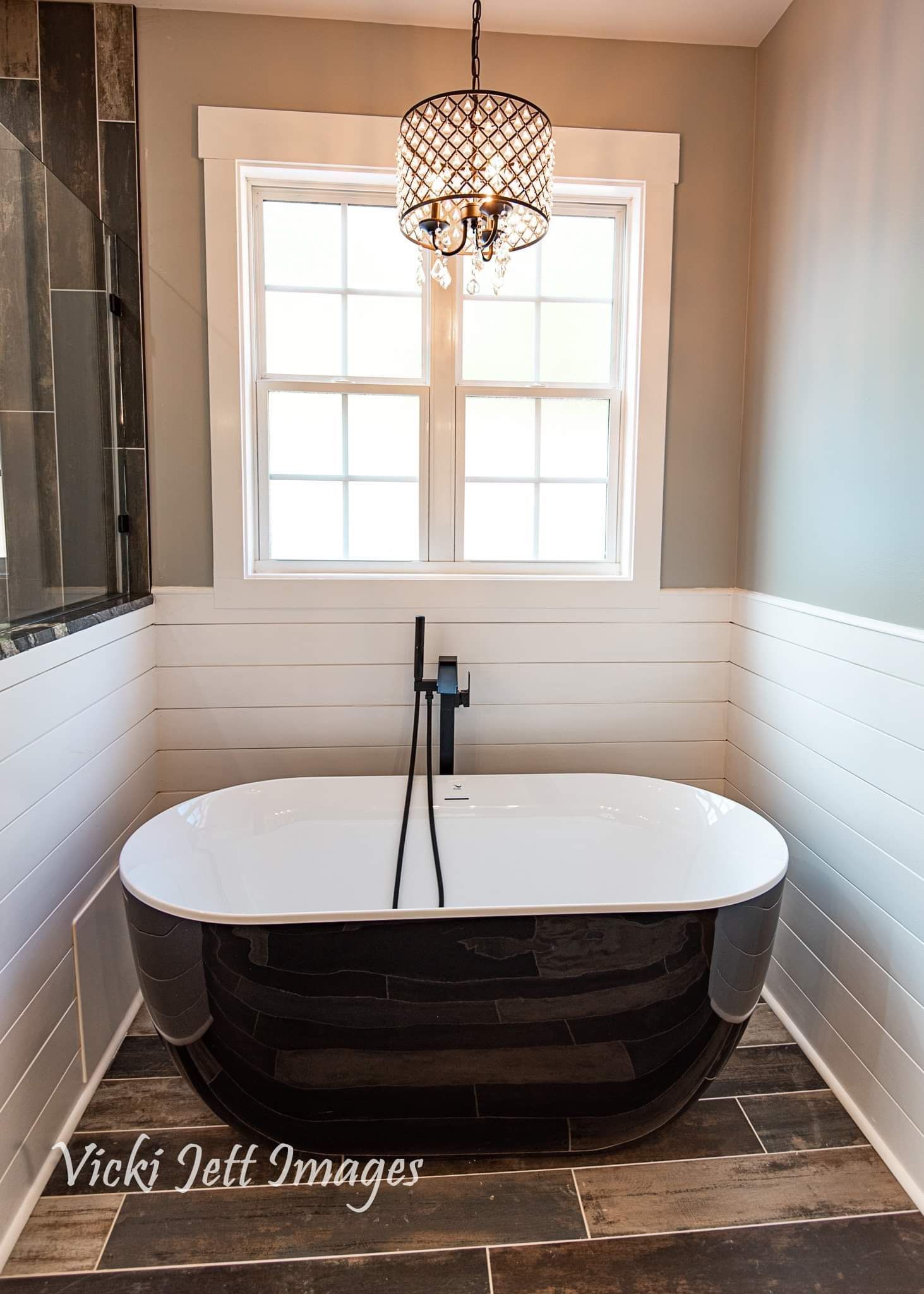 A bathtub in a bathroom with a window and a chandelier hanging from the ceiling.