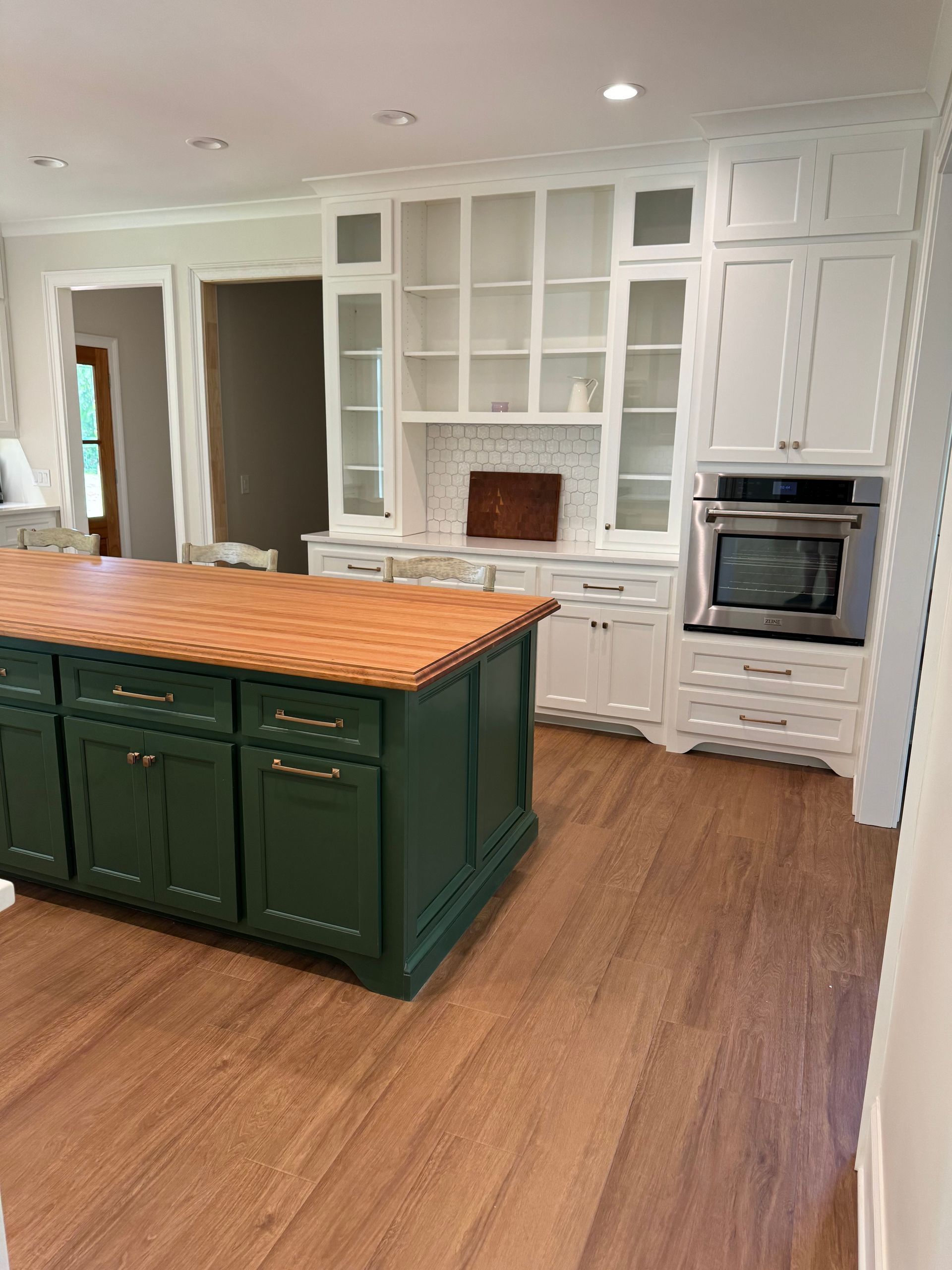 A kitchen with white cabinets and a green island with a wooden counter top.