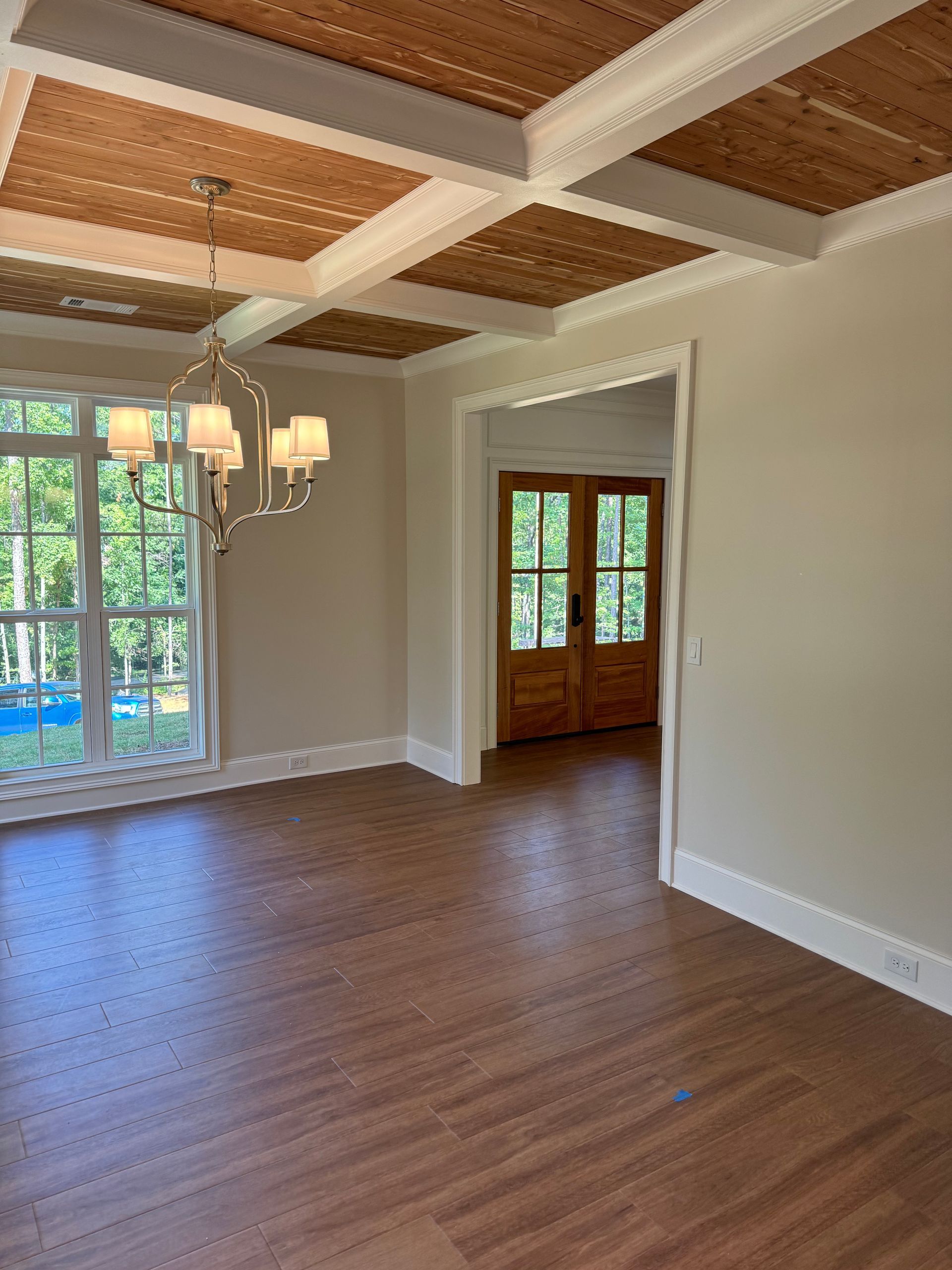 An empty dining room with hardwood floors and a chandelier.
