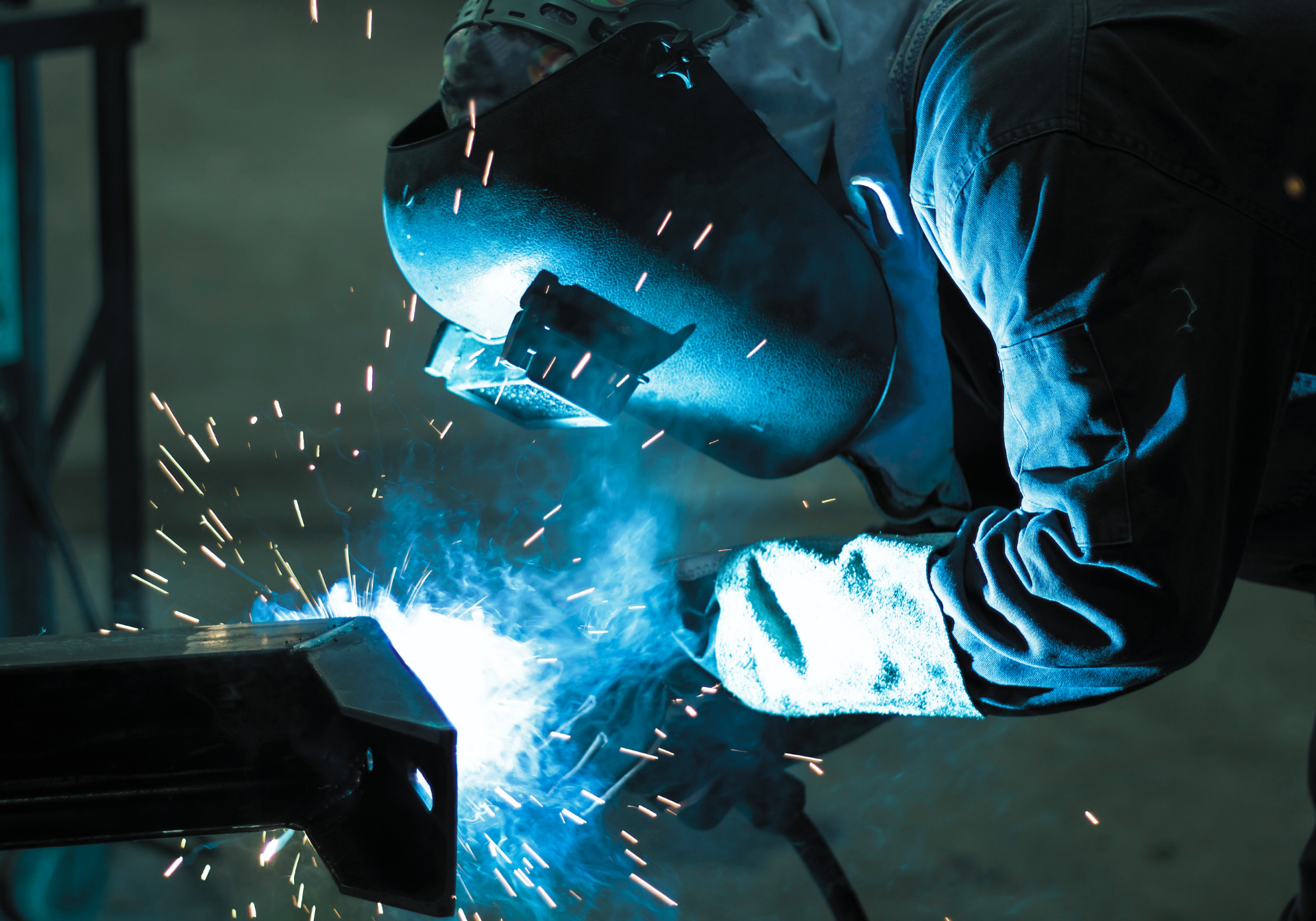Welder in protective gear welding metal, blue sparks flying.