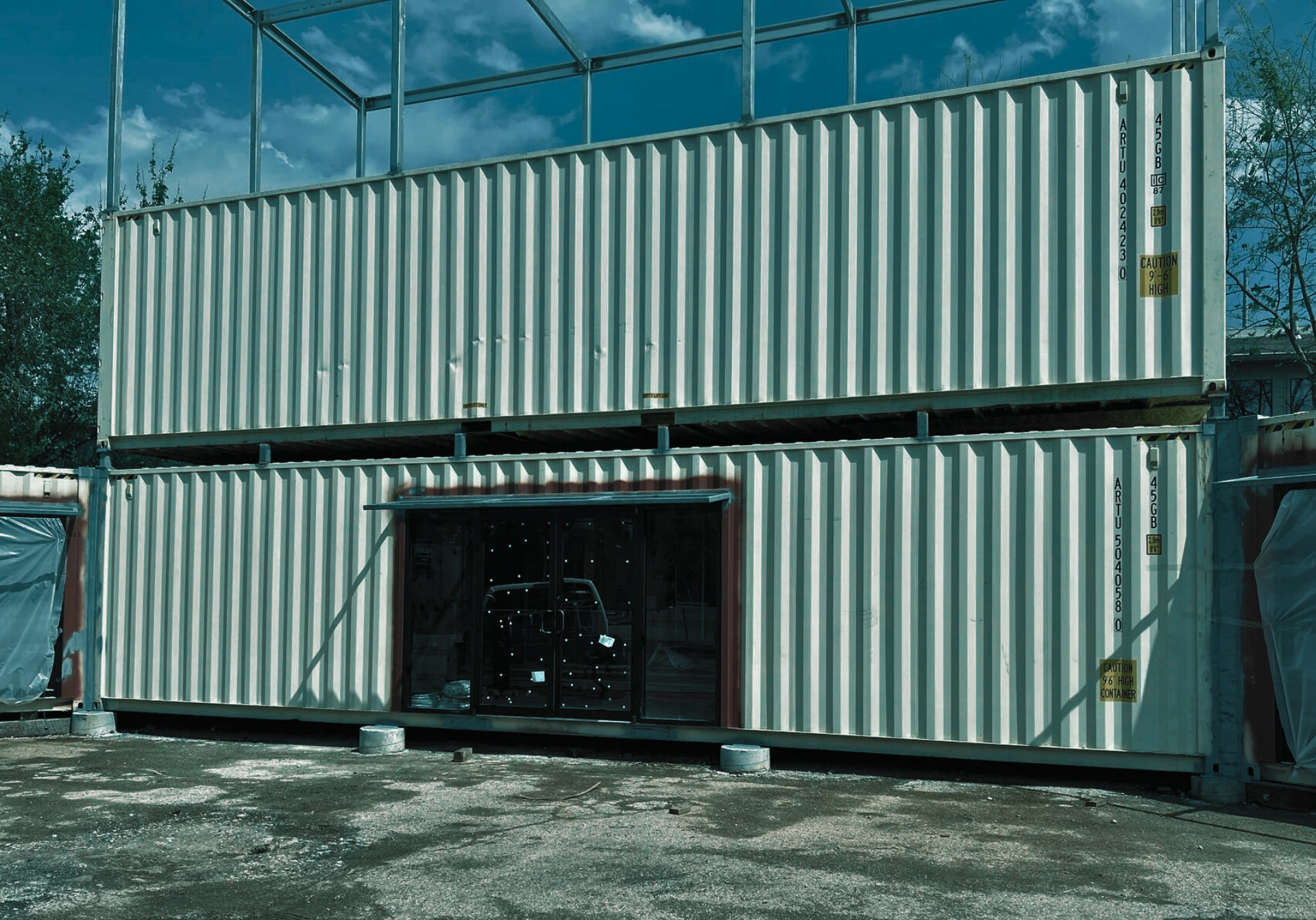 Two stacked white shipping containers with a window, under a metal frame.