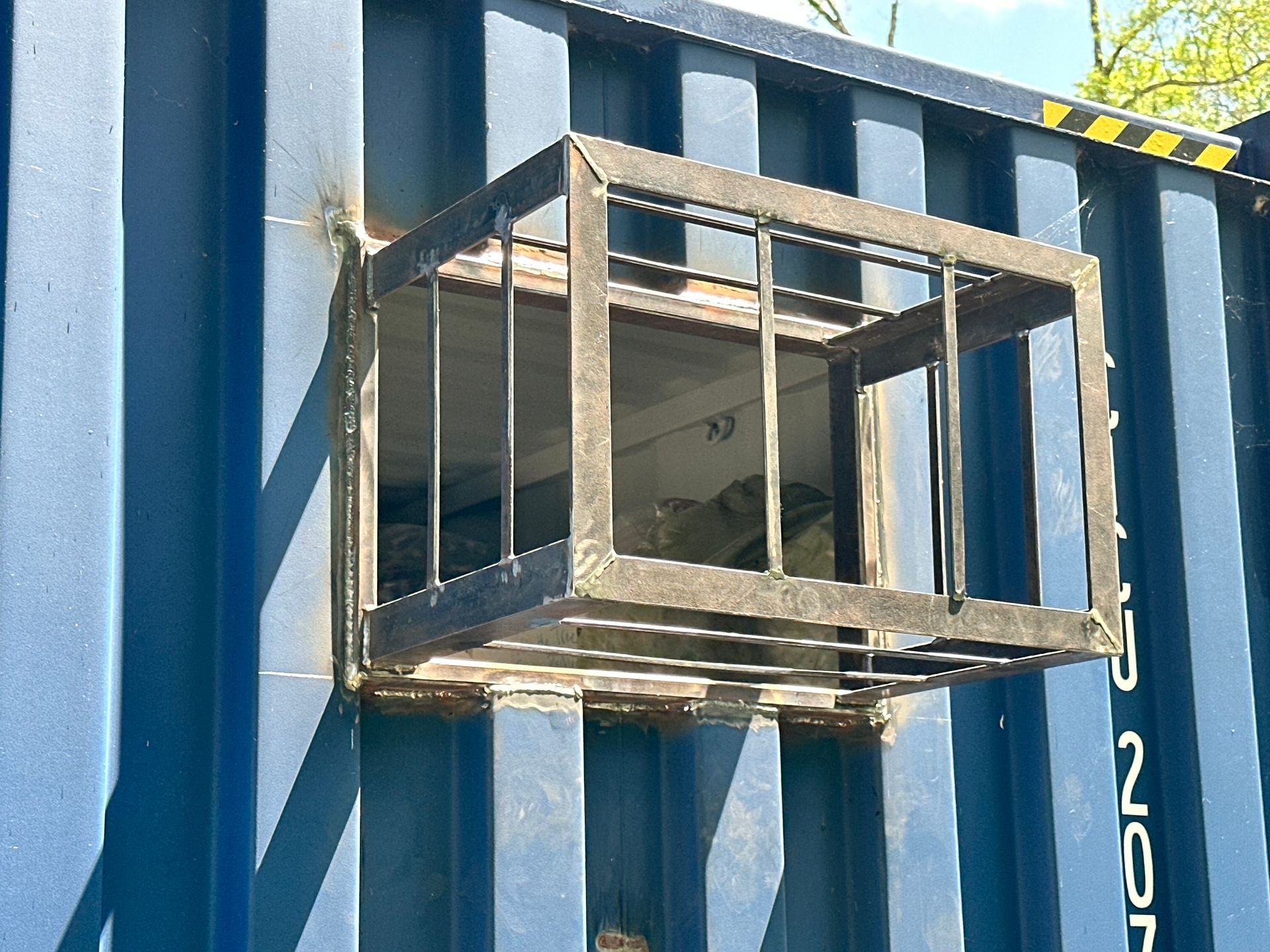 Blue shipping container with welded metal cage over a rectangular opening.