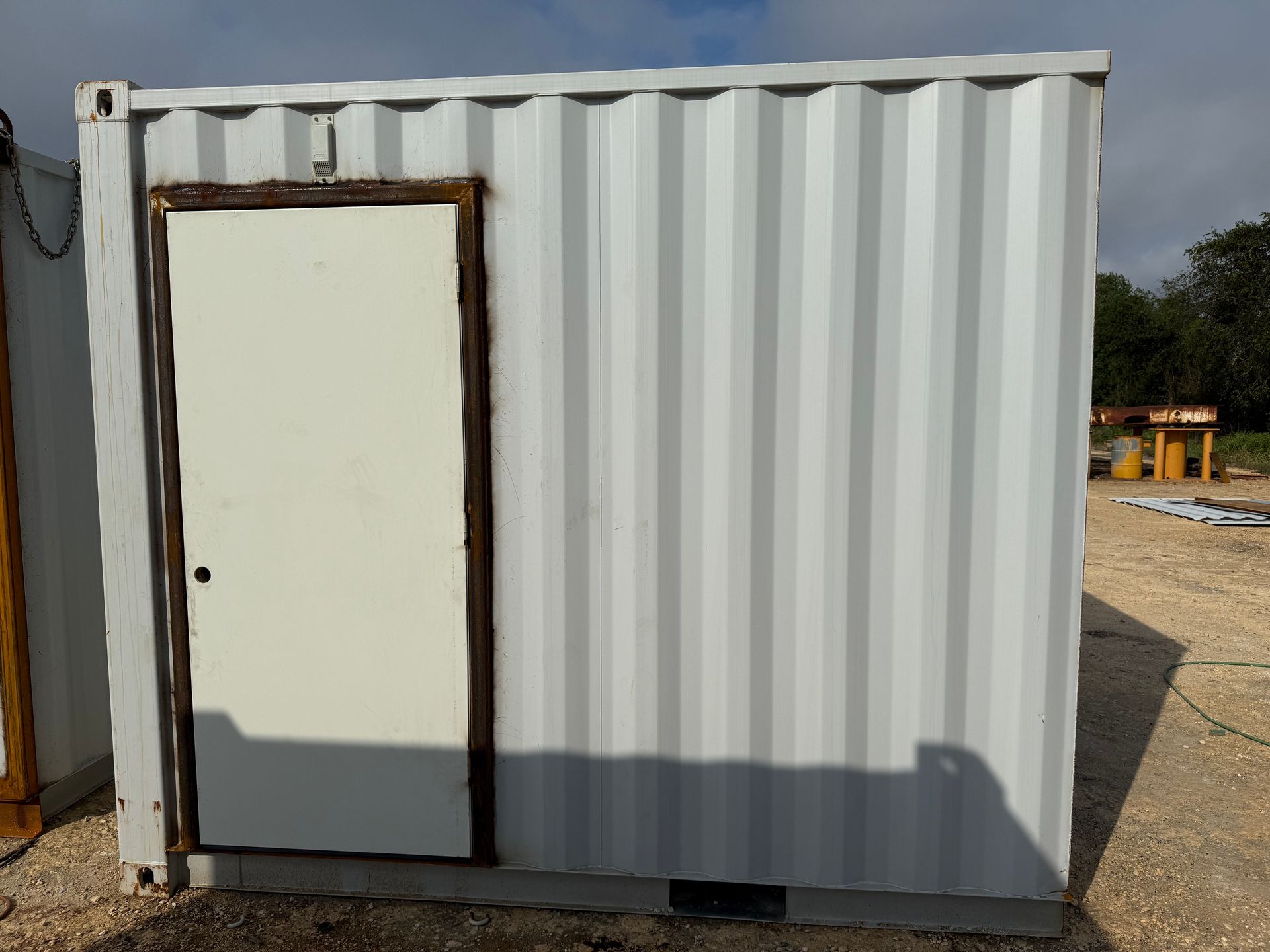 White shipping container with a white door, set outdoors under a cloudy sky.