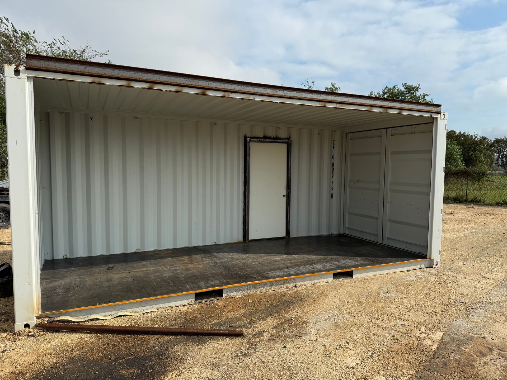 White cargo container modified with a roof and door, set on gravel.