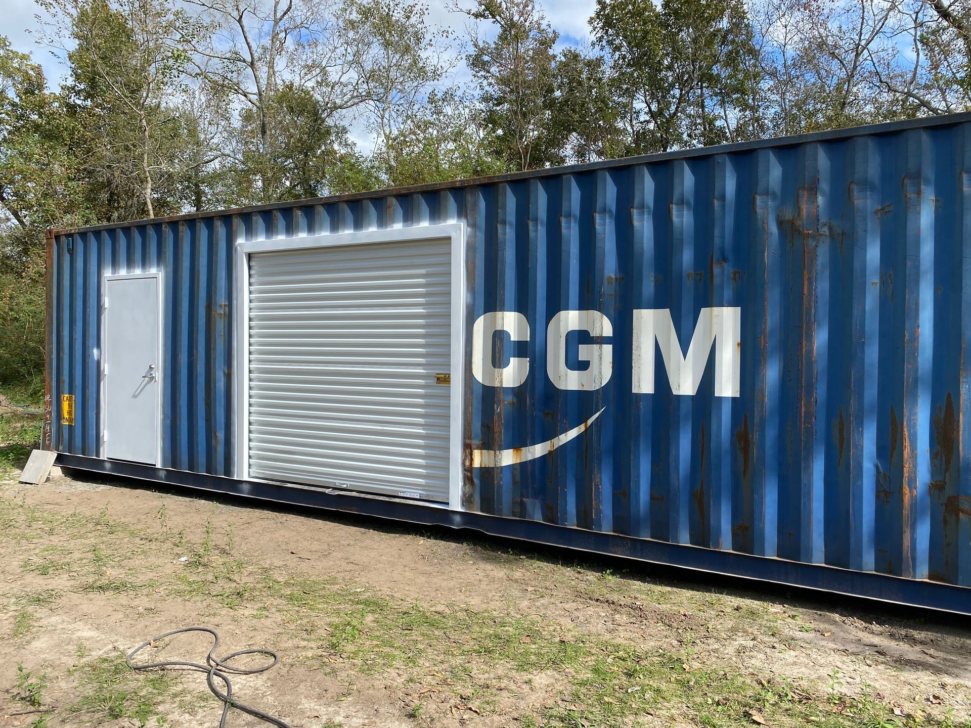Blue shipping container modified with a door, roll-up door, and the letters 