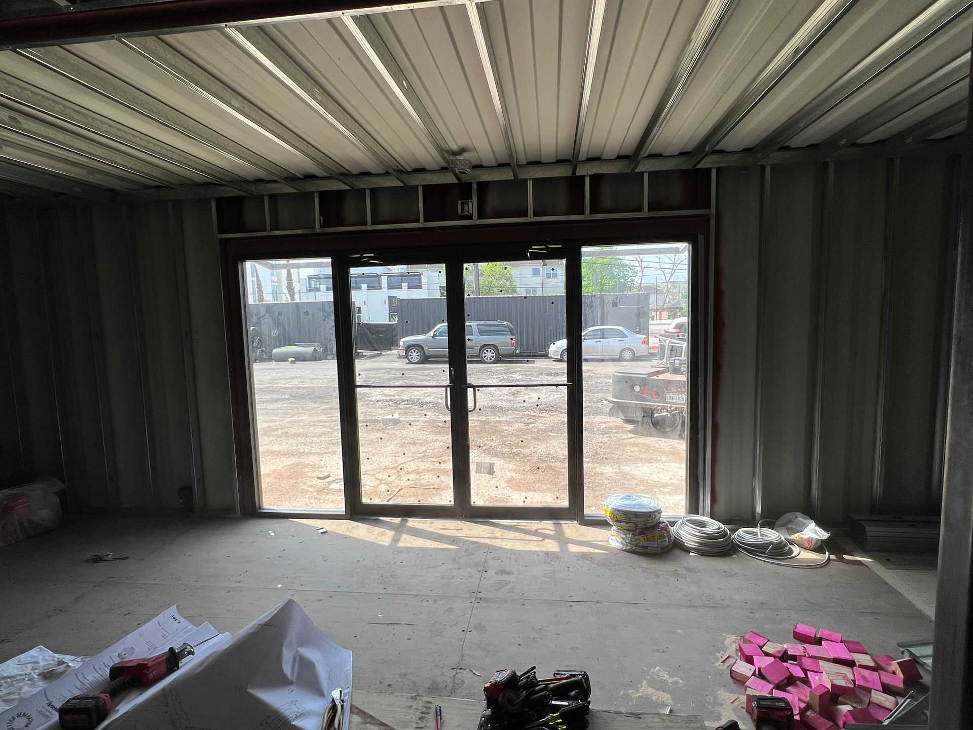 Interior view of a construction site. Metal framing and a door to the exterior with vehicles visible.