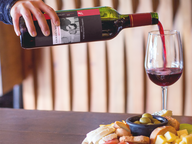 Red wine being poured into a glass, served with a charcuterie board of snacks.