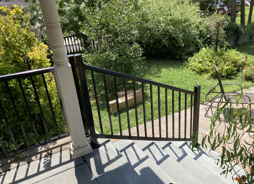 Black railing on porch steps, leading to a grassy yard with trees. Black railing on porch steps, leading to a grassy yard with trees.
