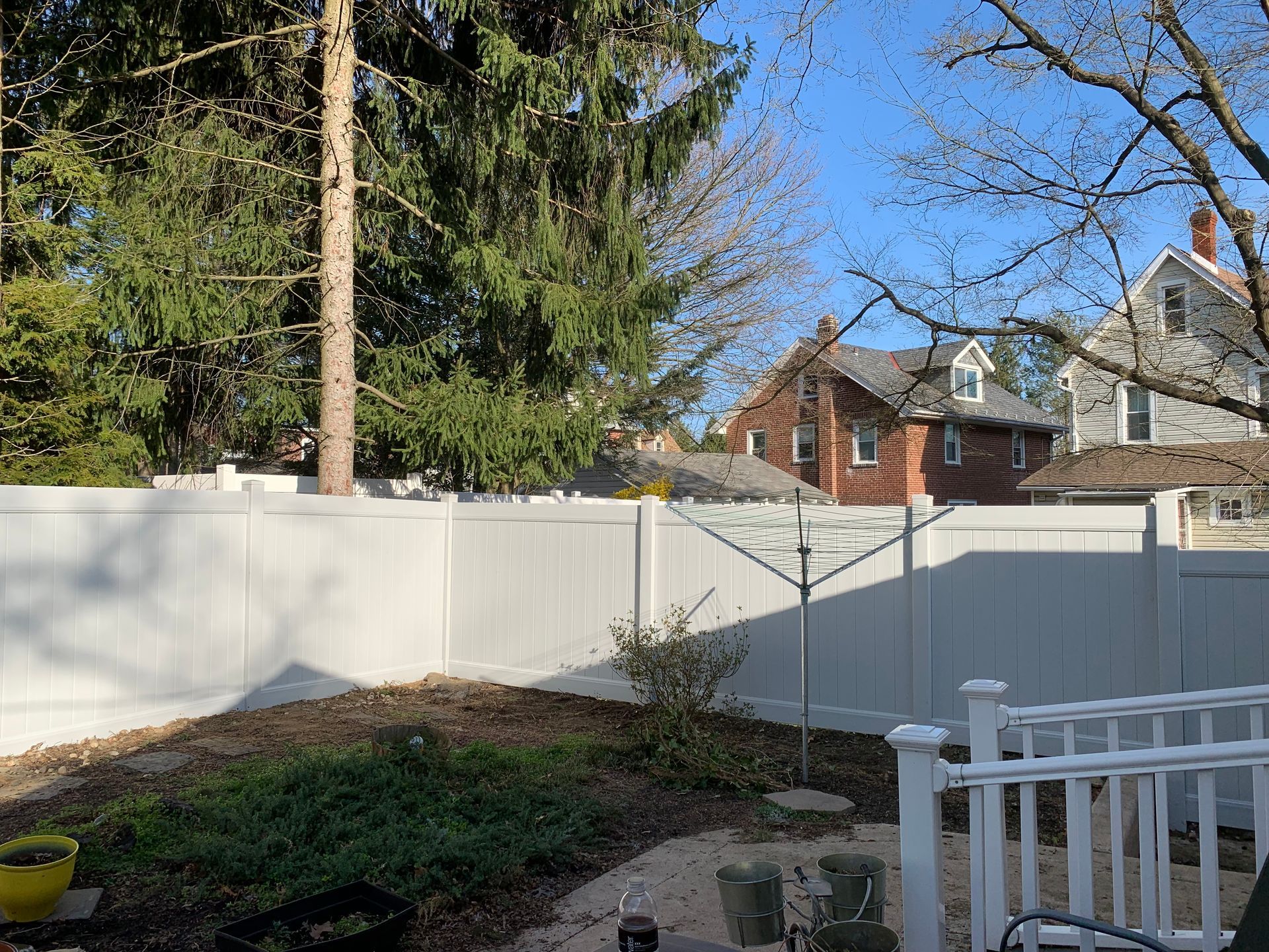 Backyard with white fence, trees, and houses in the background on a sunny day. Backyard with white fence, trees, and houses in the background on a sunny day.