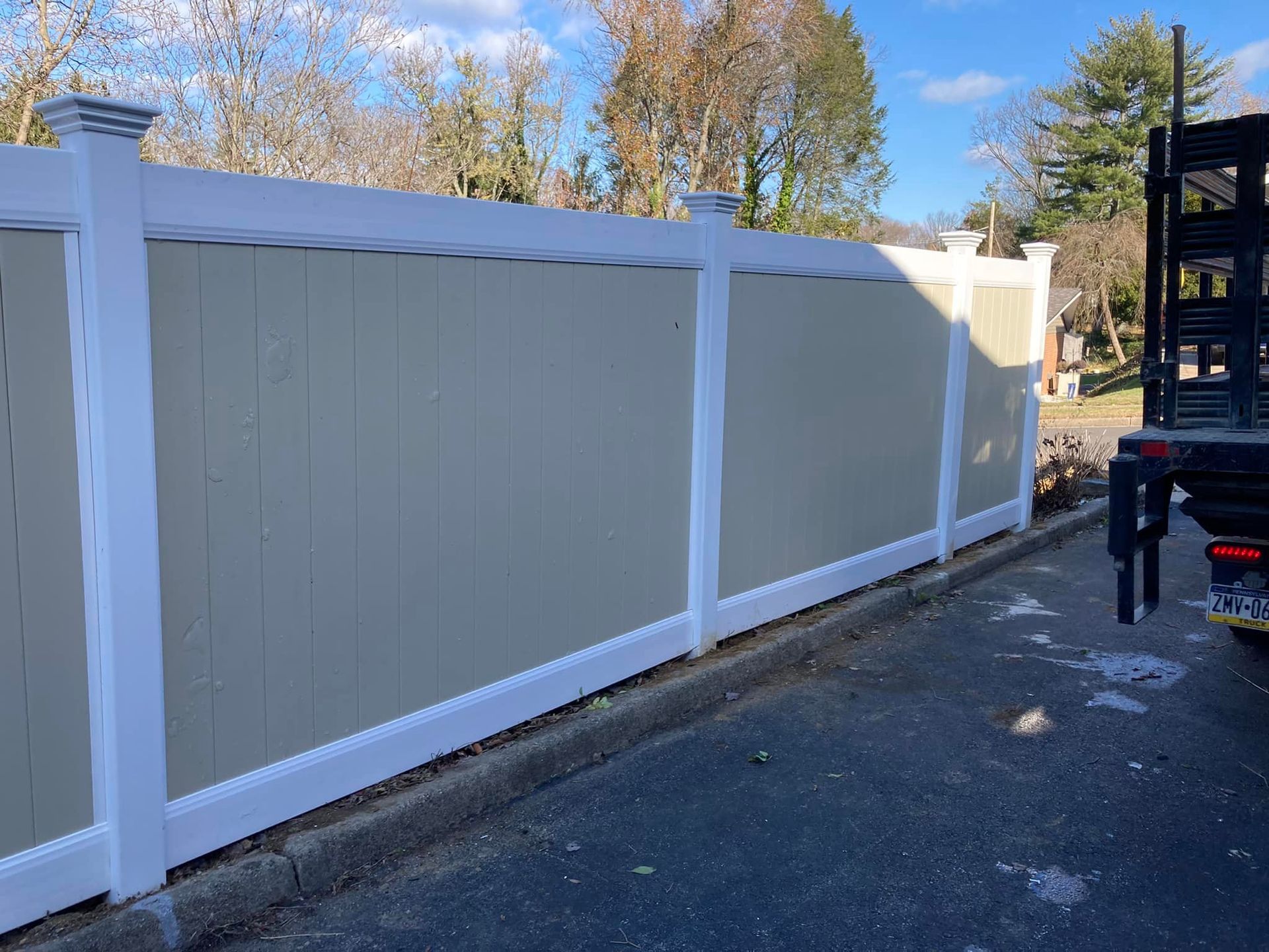 Beige vinyl fence with white trim, against a blue sky, next to a paved area. Beige vinyl fence with white trim, against a blue sky, next to a paved area.