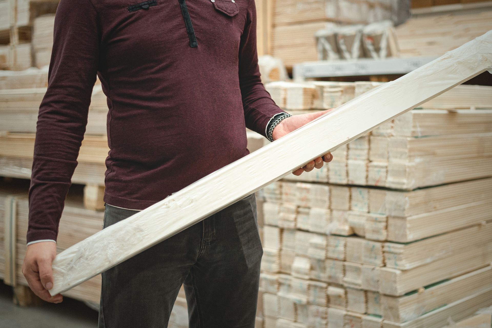 Man in burgundy shirt holding a wooden plank in a lumberyard. Man in burgundy shirt holding a wooden plank in a lumberyard.