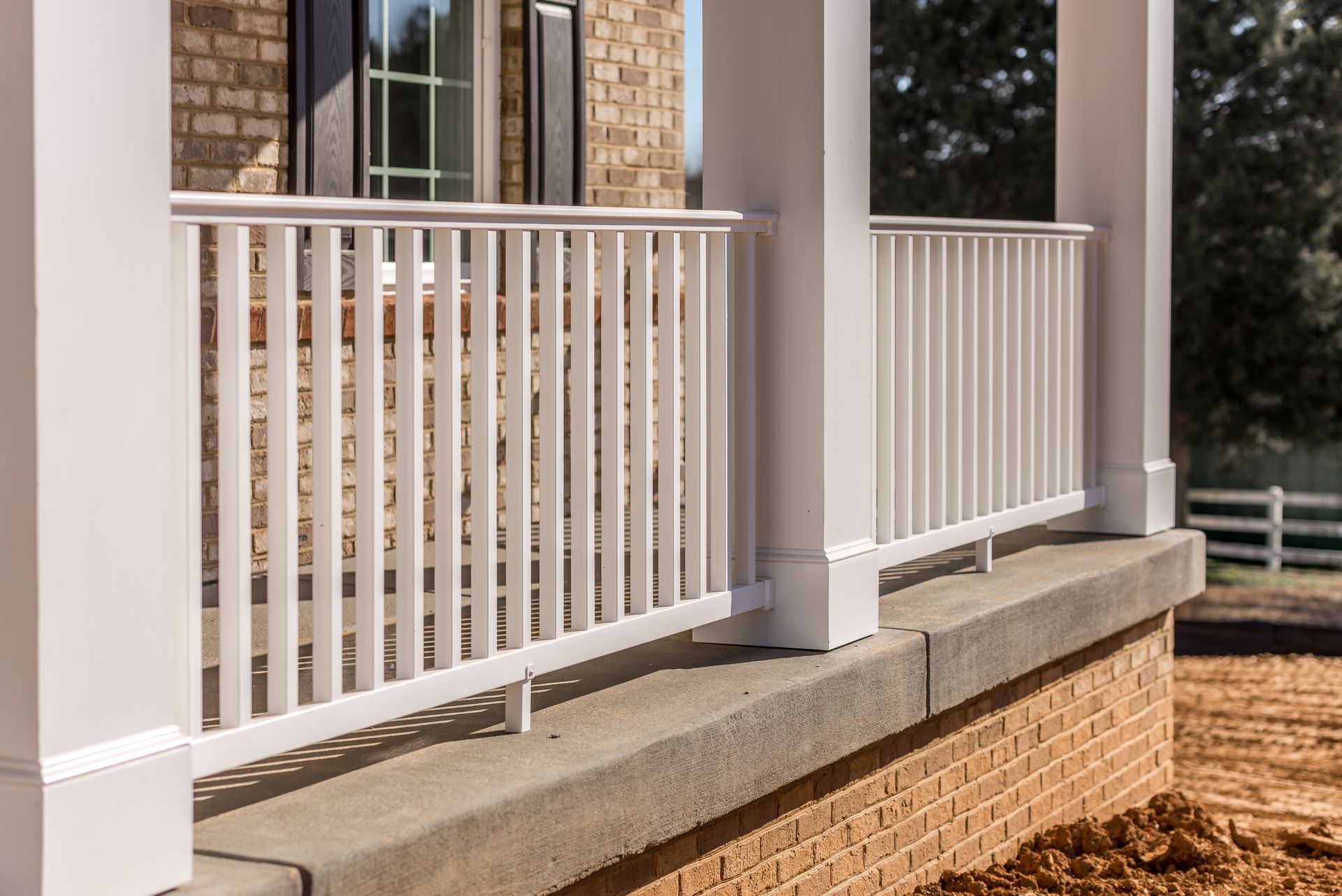 White picket fence in front of a brick house. Fence surrounds brown mulch in a neighborhood. White picket fence in front of a brick house. Fence surrounds brown mulch in a neighborhood.