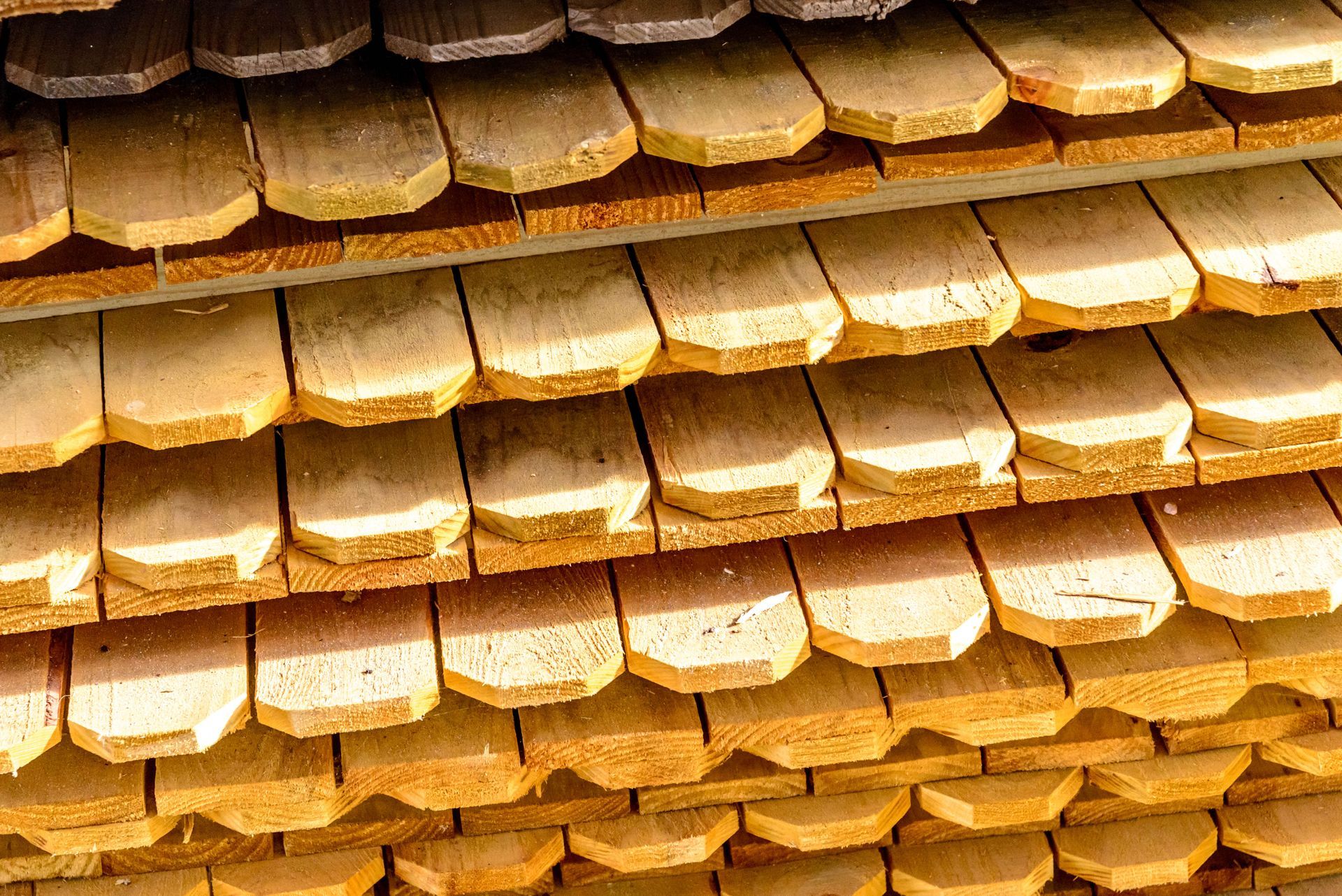 Stack of wooden shingles, light brown, with rounded ends, ready for use.