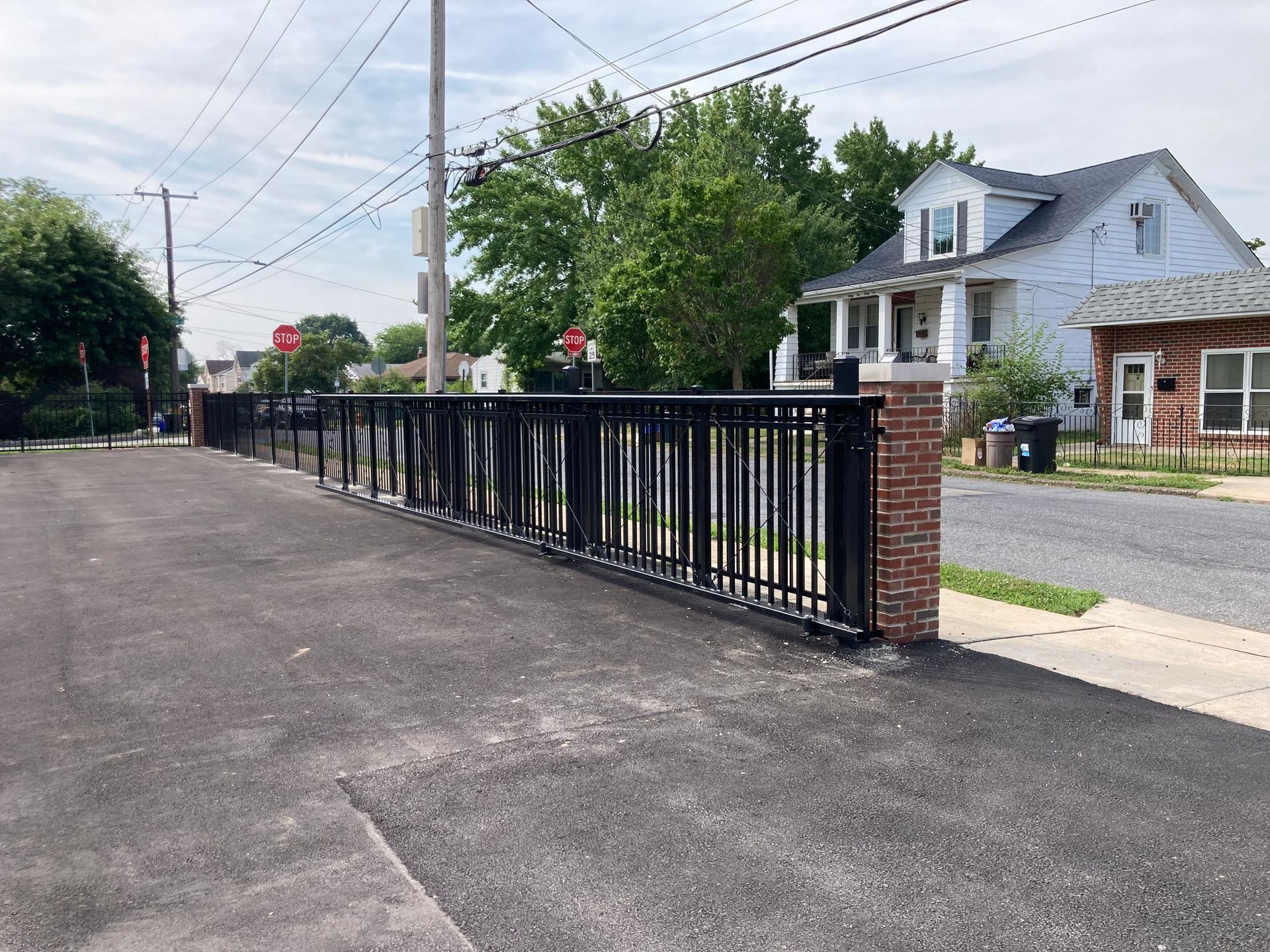 Black metal fence along paved area with street and houses.