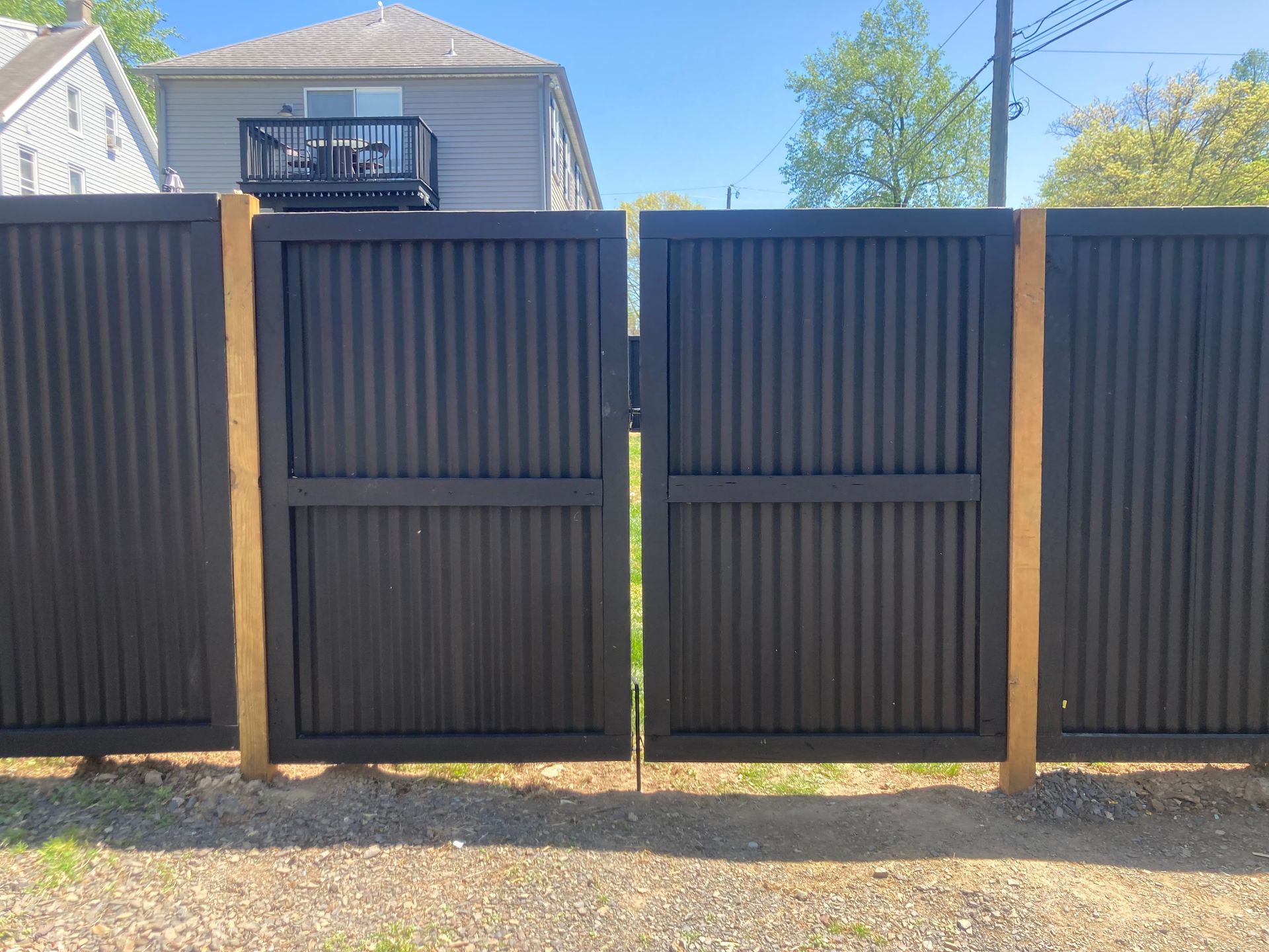 Black corrugated metal gate in wooden posts, exterior.