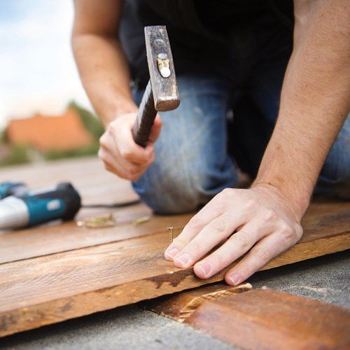 worker hammering nail onto wood deck
