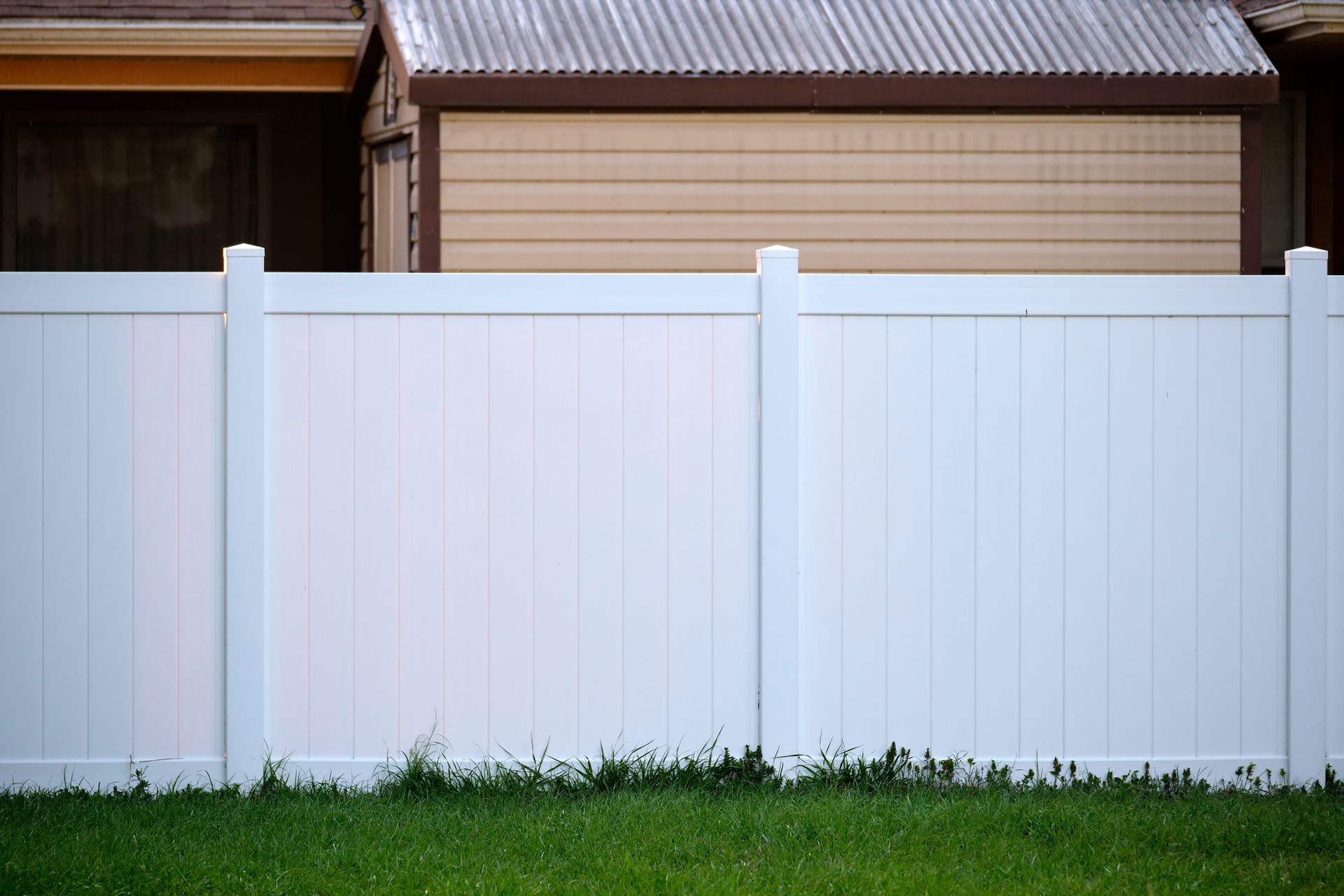 A white fence surrounds a lush green yard in front of a house.