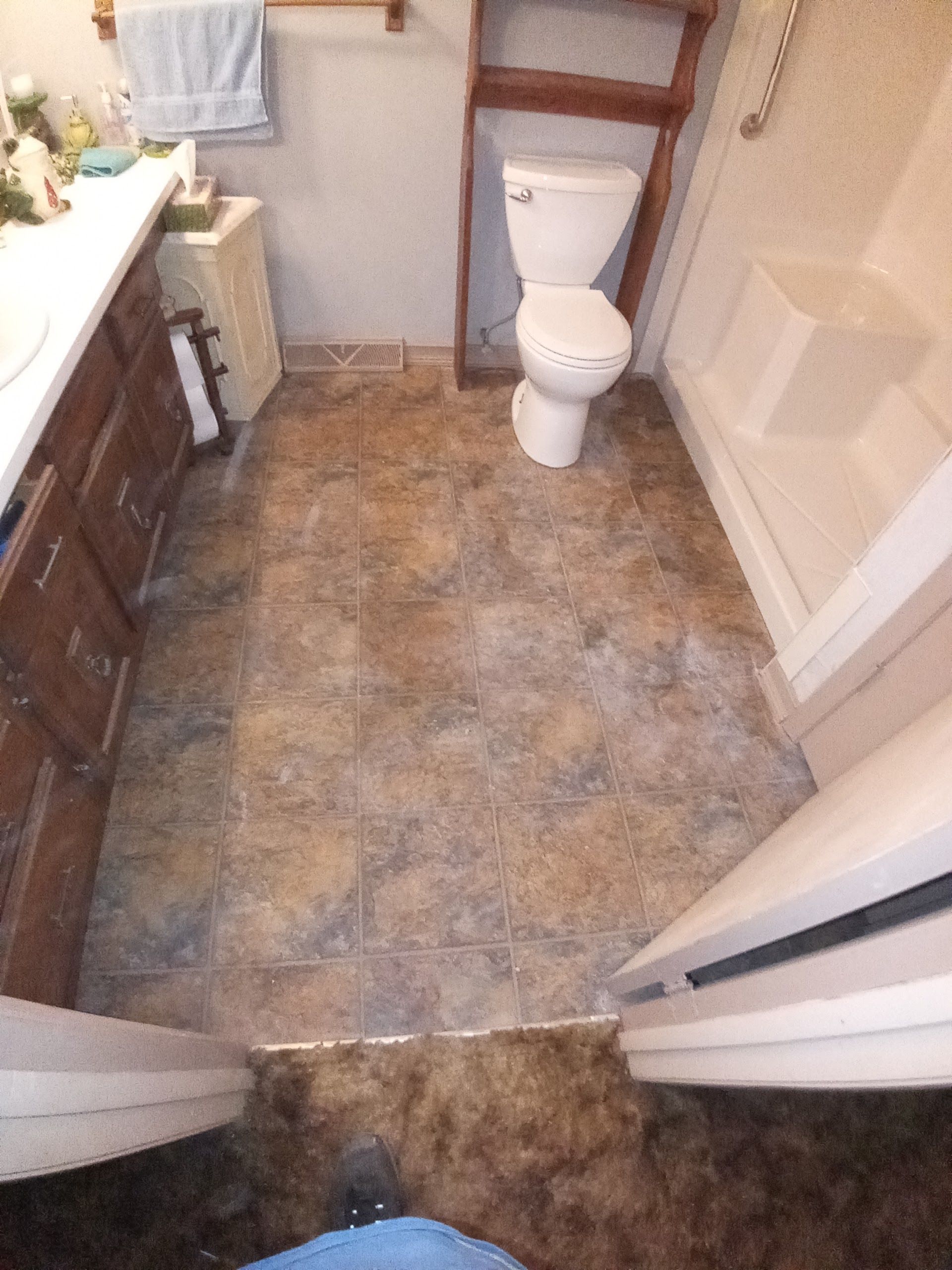A high-angle view of a bathroom with stone-look tile flooring, a white toilet, a wooden vanity, and a shower stall.
