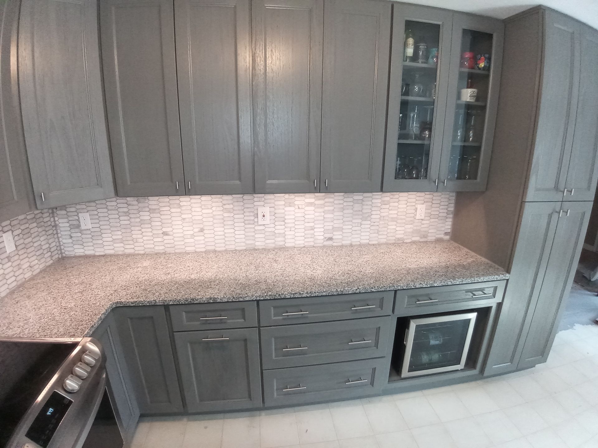 A kitchen featuring grey cabinets, granite countertops, a tiled backsplash, and a built-in wine cooler.
