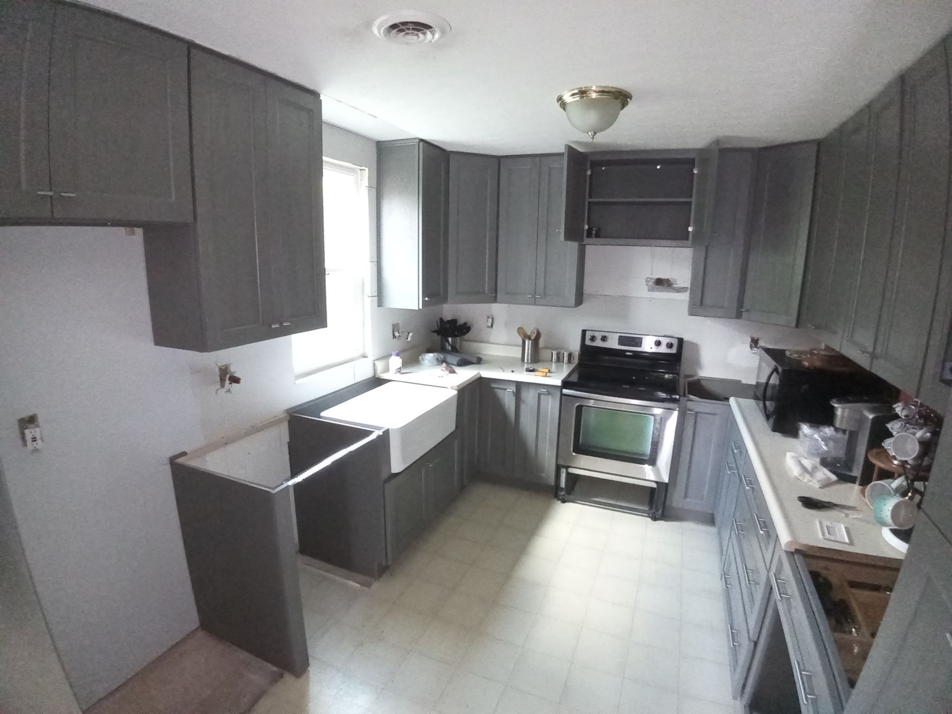 A kitchen featuring grey cabinets, an open-concept layout, a white farmhouse sink, and a black stove.
