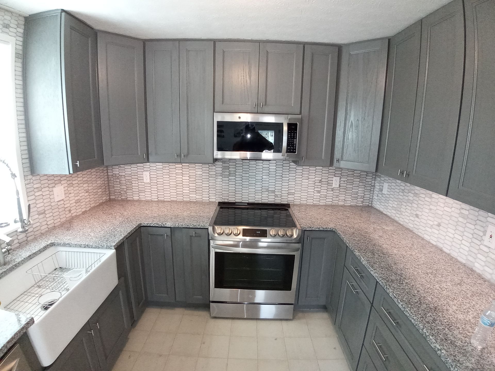 A kitchen with gray cabinets, granite countertops, a white farmhouse sink, and stainless steel stove and microwave.