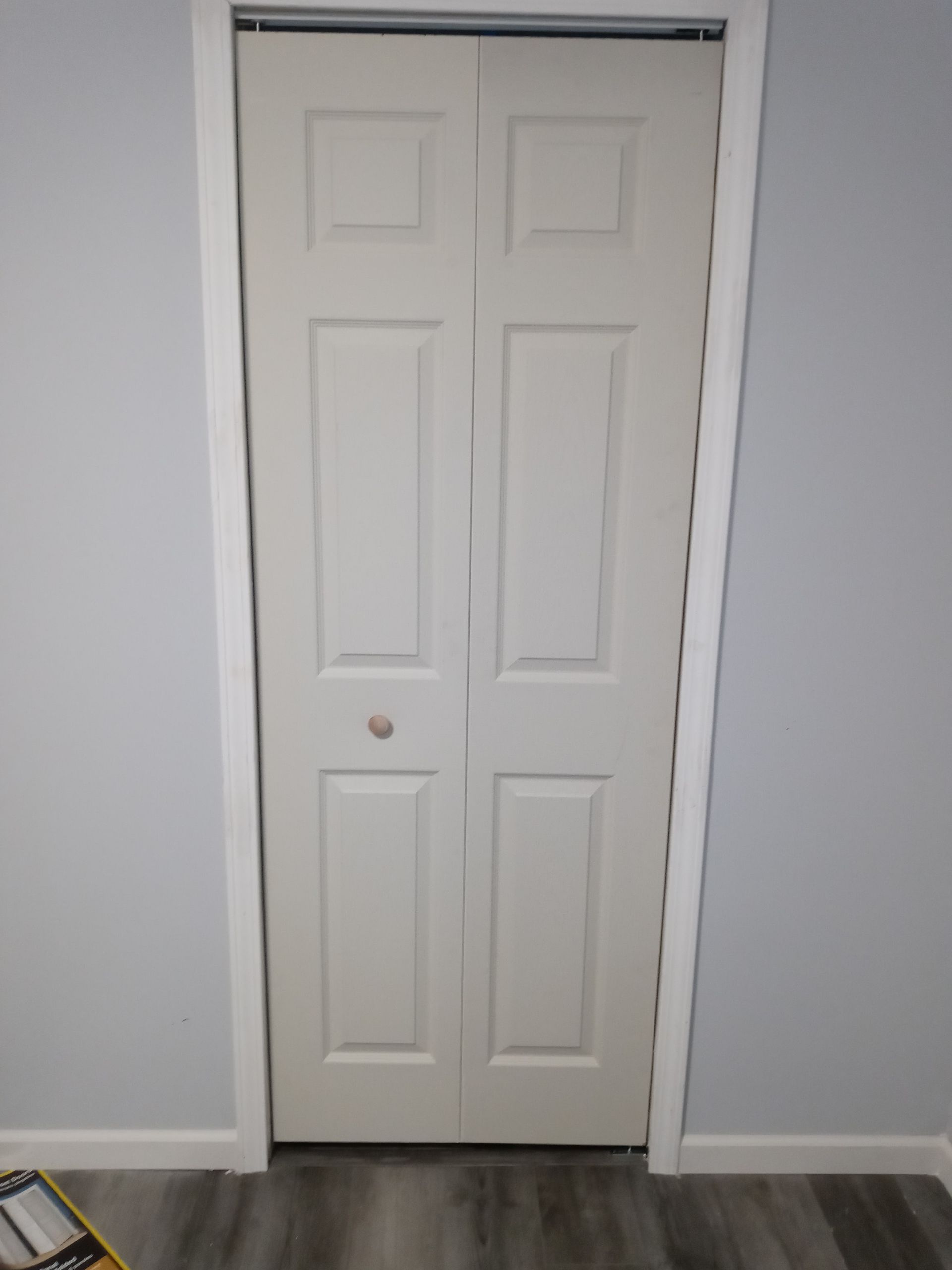 A white, six-panel bifold door installed in a light blue room with gray wood-look flooring.