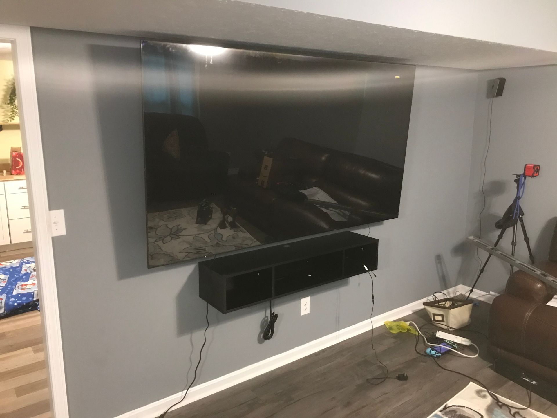 A large flat-screen TV mounted on a gray wall above a black floating shelf in a basement living area.