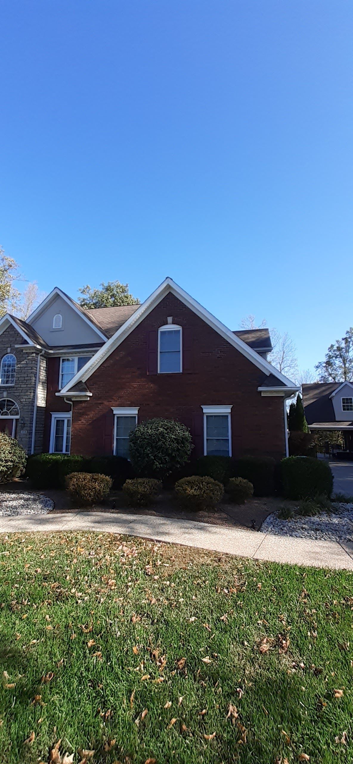 A two-story brick house with a gabled roof and arched attic window, viewed from a lawn under a clear blue sky.