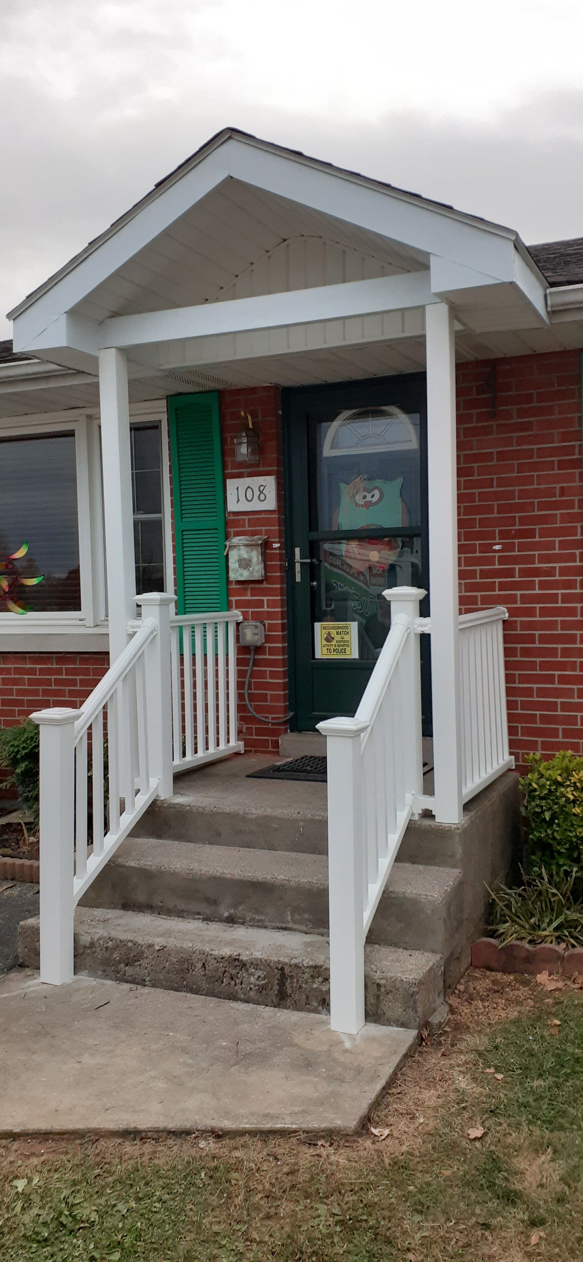 A red brick house entrance featuring a white covered porch, steps with white railings, and a green front door.