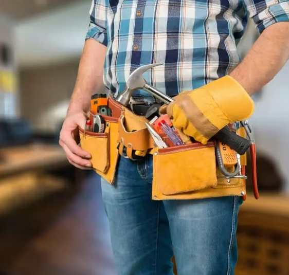 A person wearing a blue plaid shirt, jeans, and a tool belt stocked with hand tools, including a hammer.