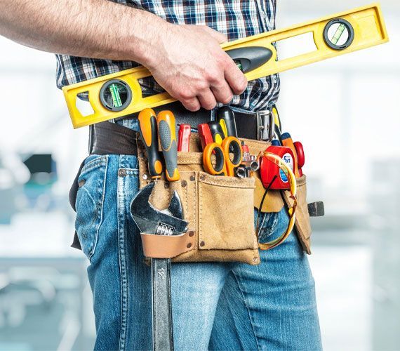 A person wearing a tool belt filled with various hand tools, holding a yellow spirit level against their waist.