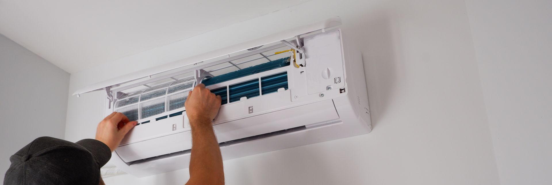 Des mains nettoient un filtre de climatiseur mural avec un chiffon bleu.