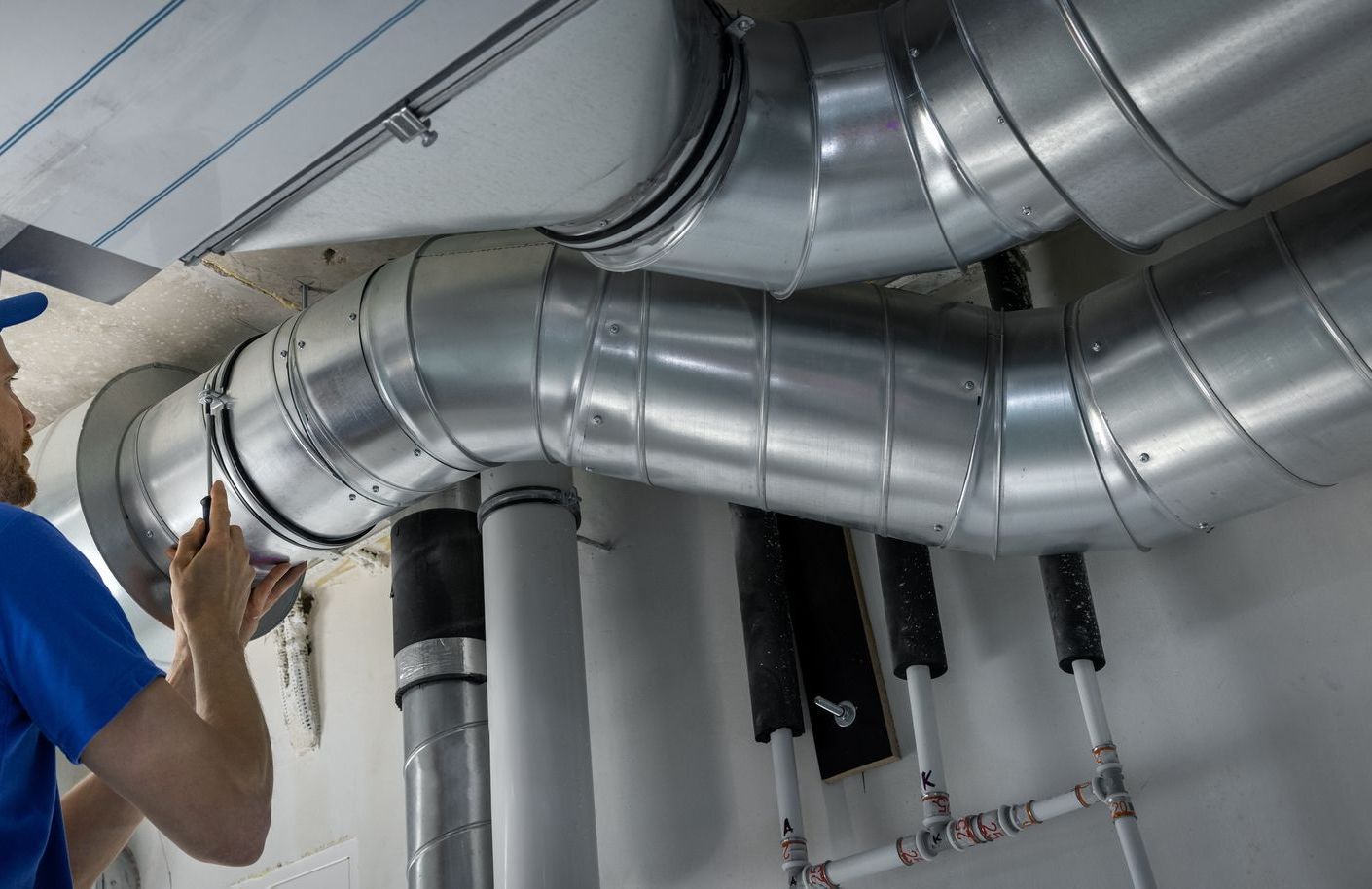 Ouvrier installant des conduits de ventilation en métal brillant dans un espace sous plafond