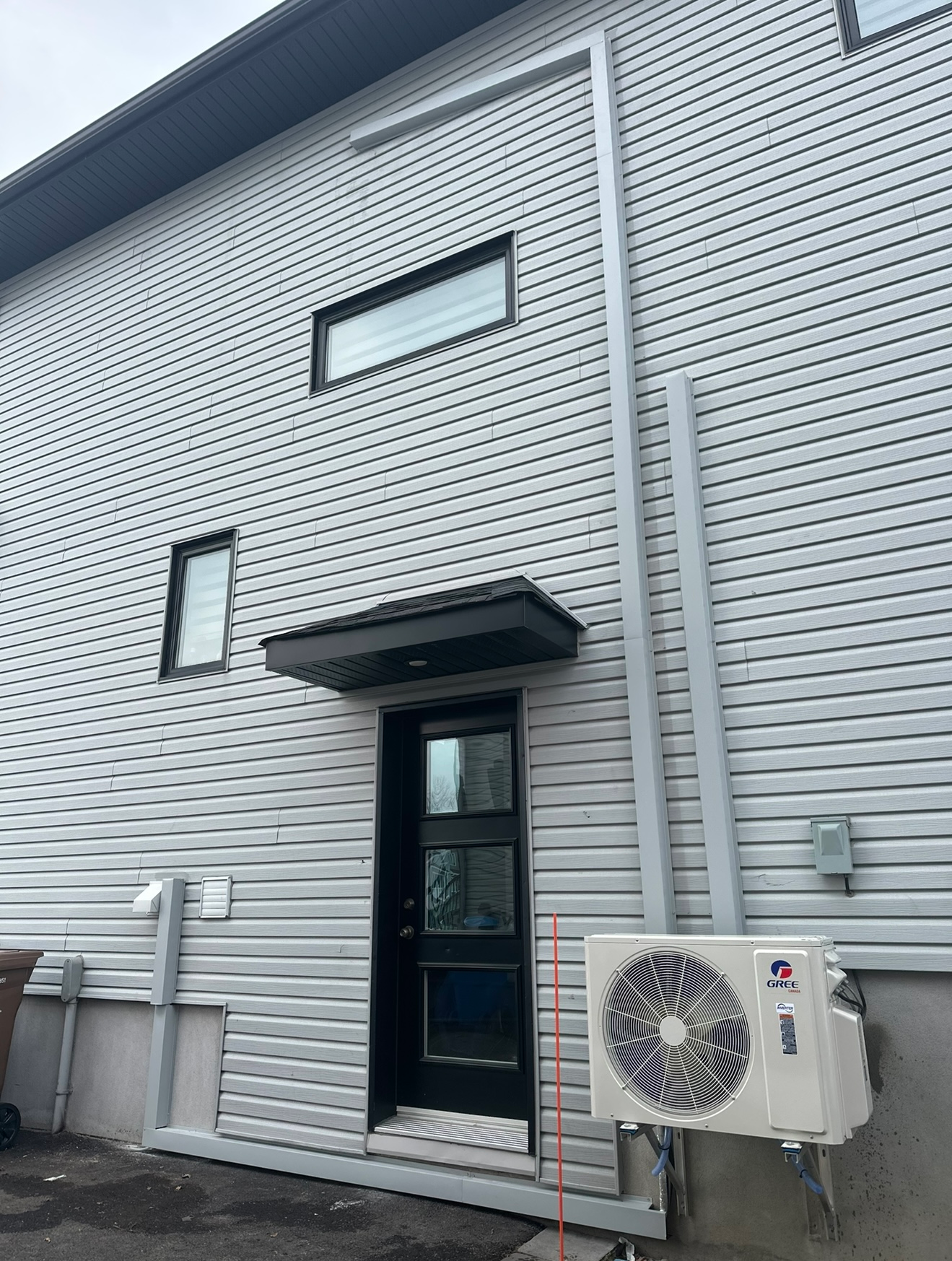 Une maison blanche avec une porte noire et un climatiseur blanc sur le côté.