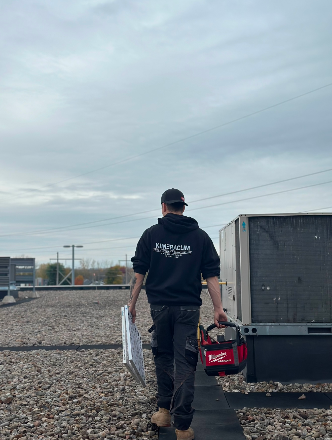 Un homme porte une boîte à outils et un morceau de papier tout en marchant sur un chemin de gravier.