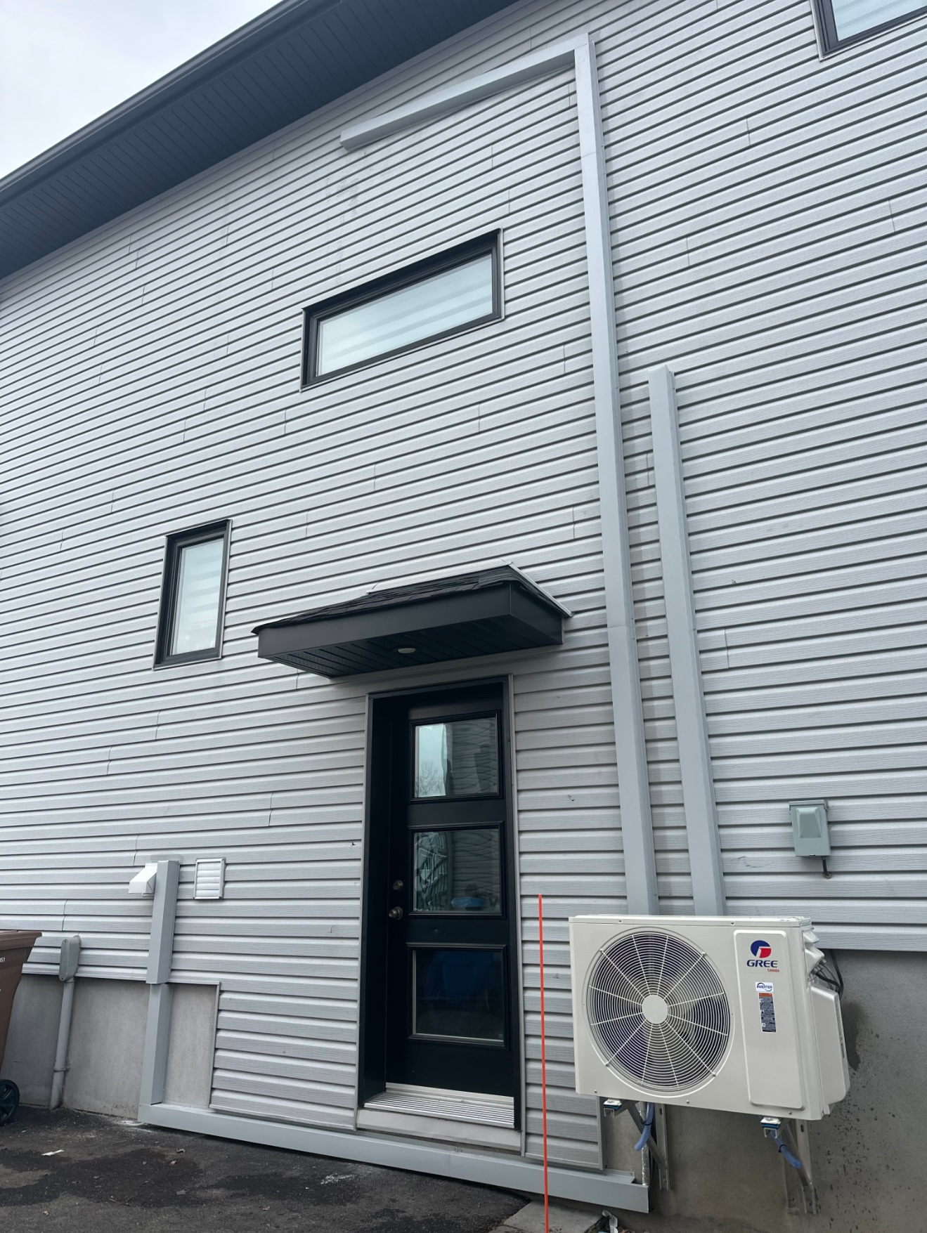 Une maison blanche avec une porte noire et un climatiseur blanc sur le côté.