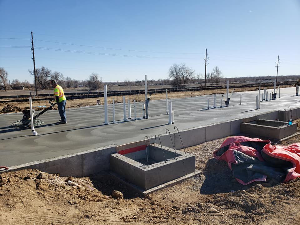 A construction worker operates a power trowel on a newly poured concrete slab at an outdoor job site.