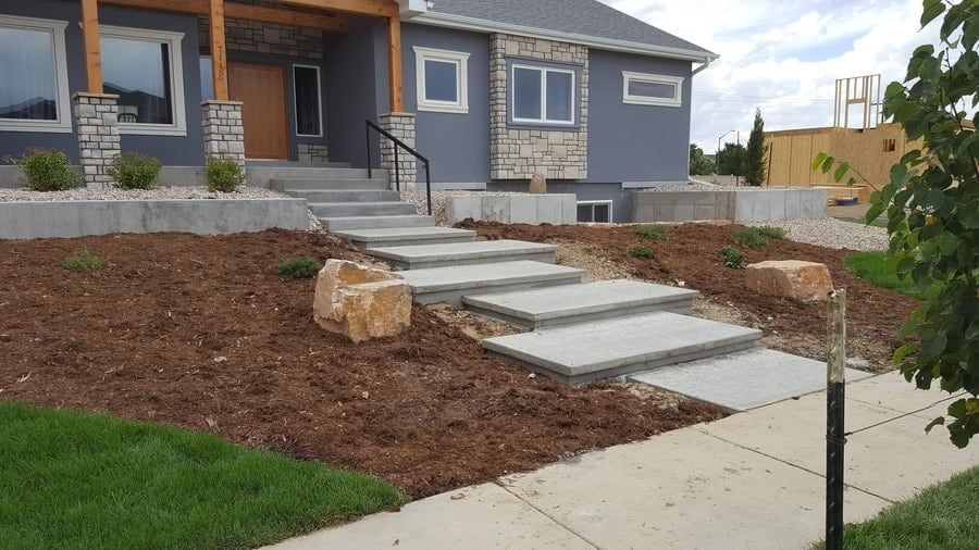 A modern house exterior with gray siding, stone accents, and concrete stairs leading up to a wooden-pillared porch.