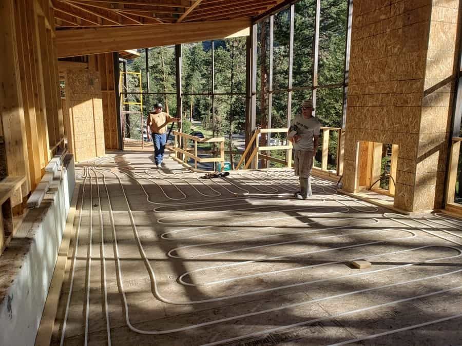 Two construction workers in an unfinished wooden building with radiant heating tubing installed on the floor.
