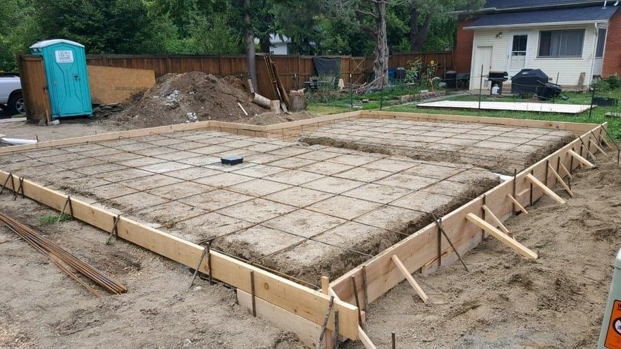 A construction site showing a concrete foundation prepared with wooden forms and metal reinforcement grid for a new build.