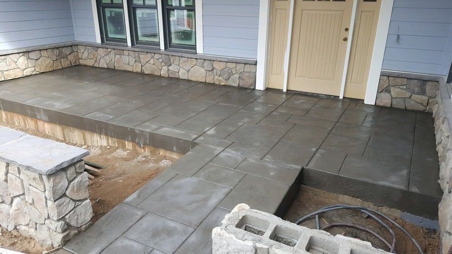 A front porch with grey stone pavers and matching stone accents under the windows, viewed from the walkway.