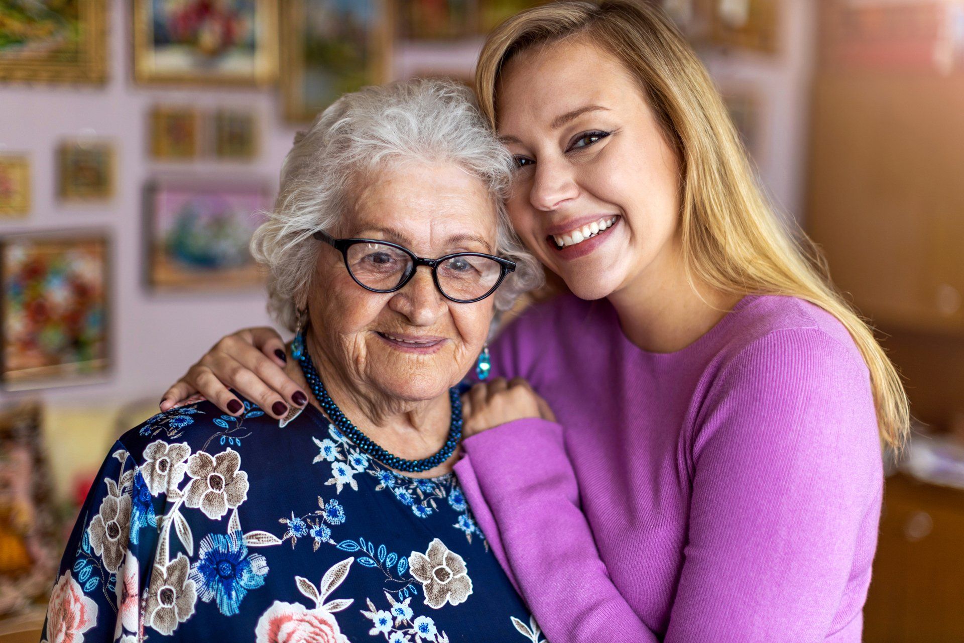A young woman is hugging an older woman who is wearing glasses.