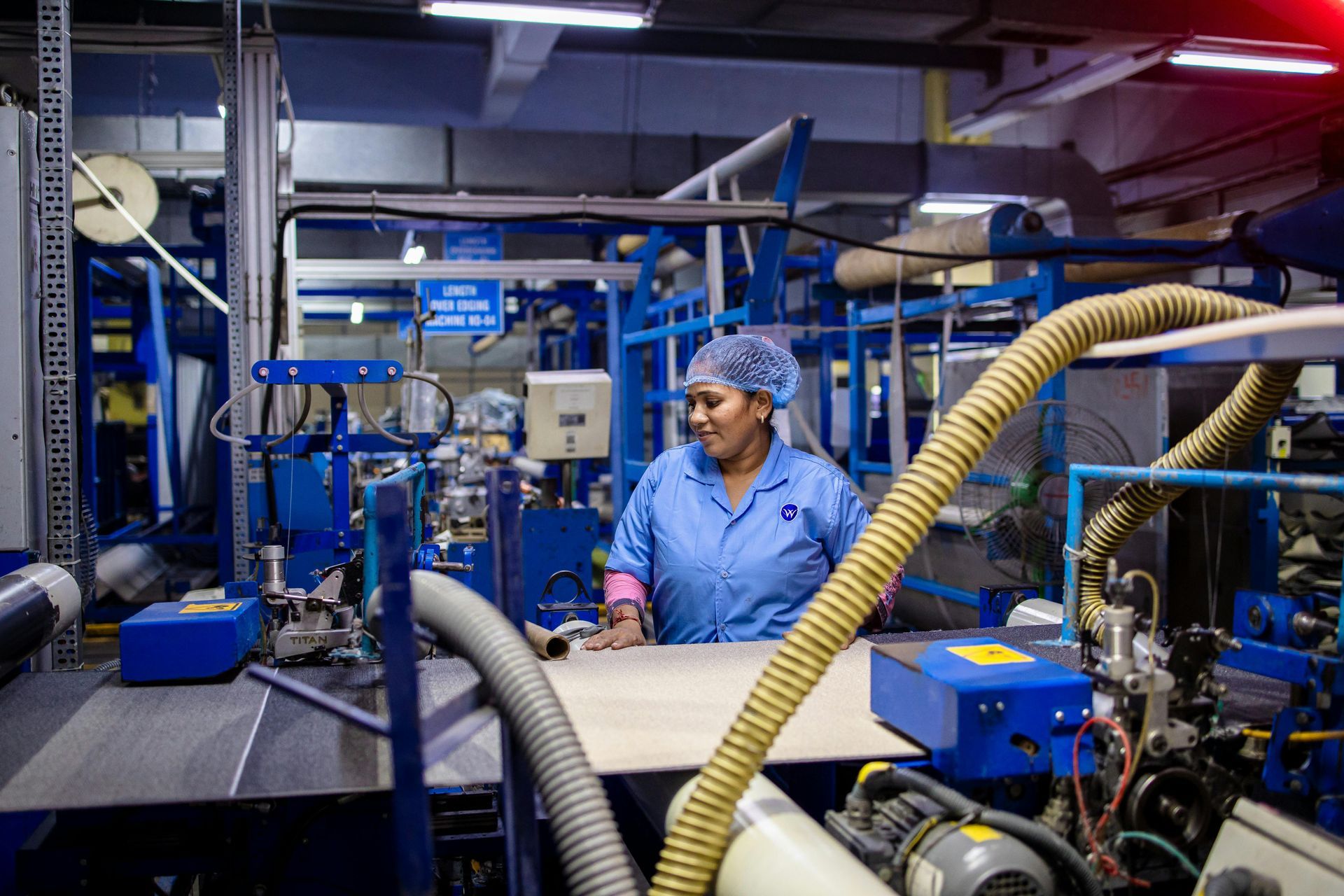 Worker in blue coveralls inspecting machinery in an industrial factory with blue equipment and hoses