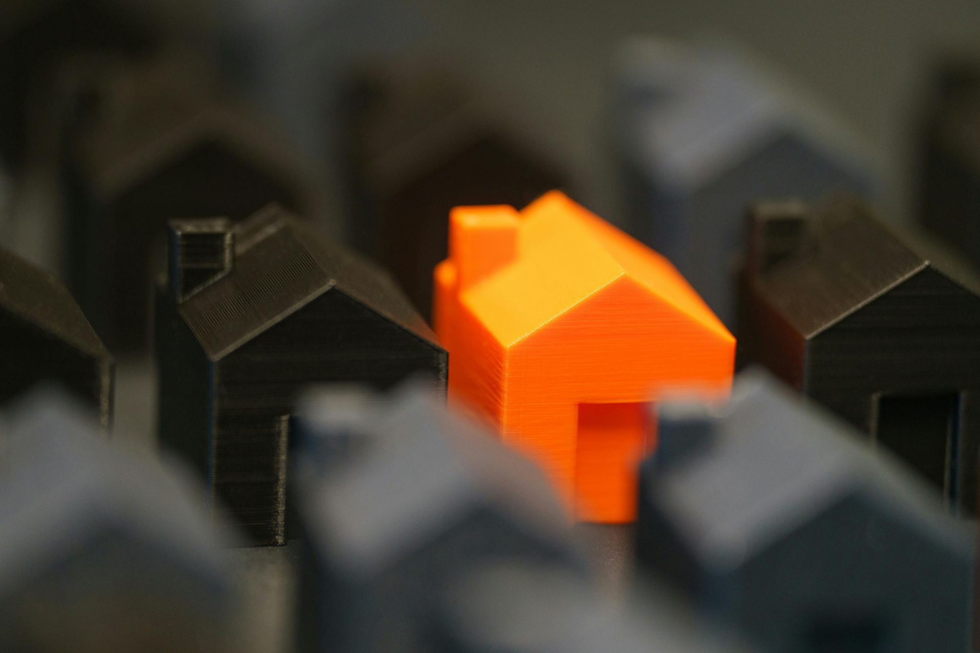 Bright orange house model among dark gray house models on a blurred background