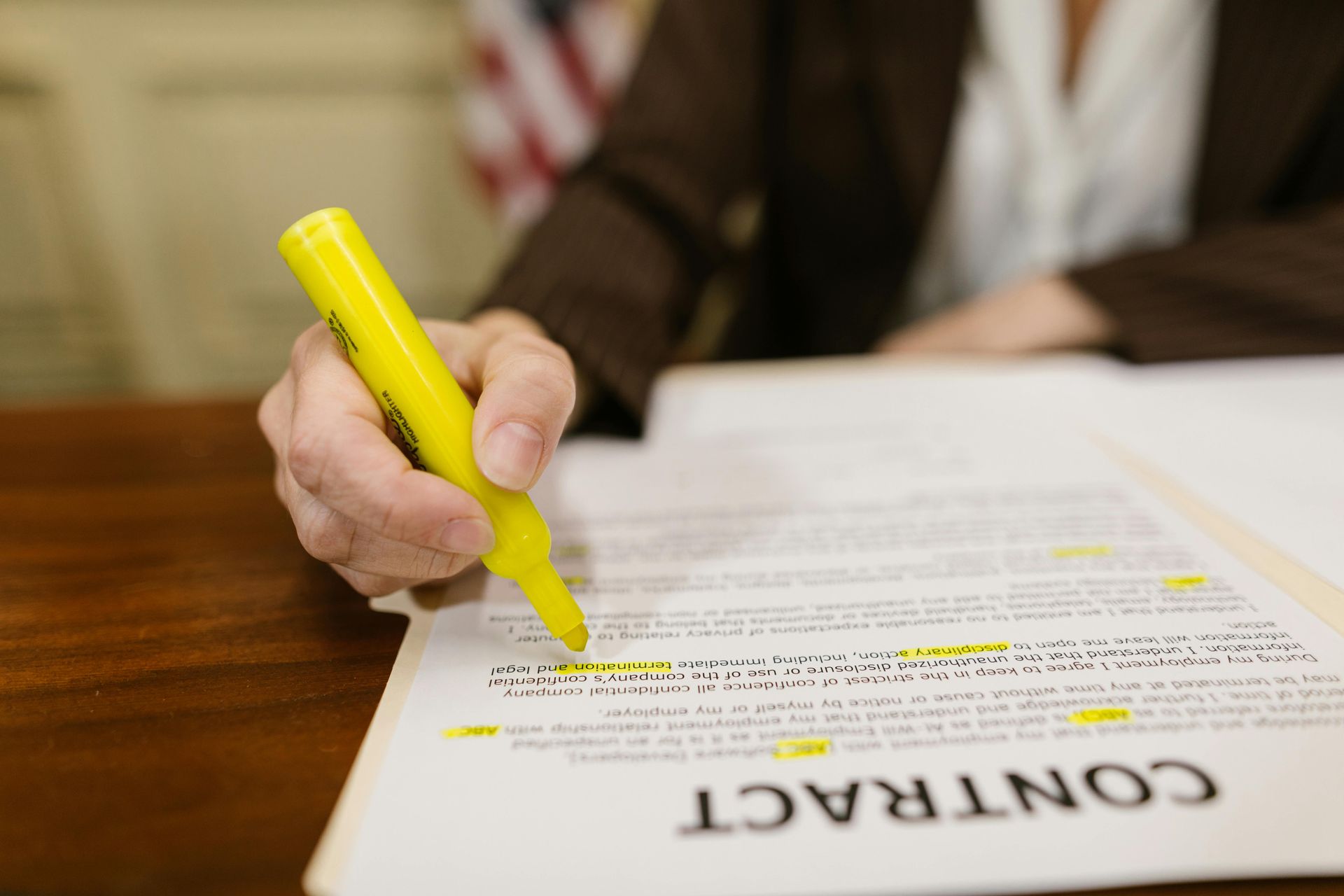 Person using a yellow highlighter to mark a contract document on a wooden table