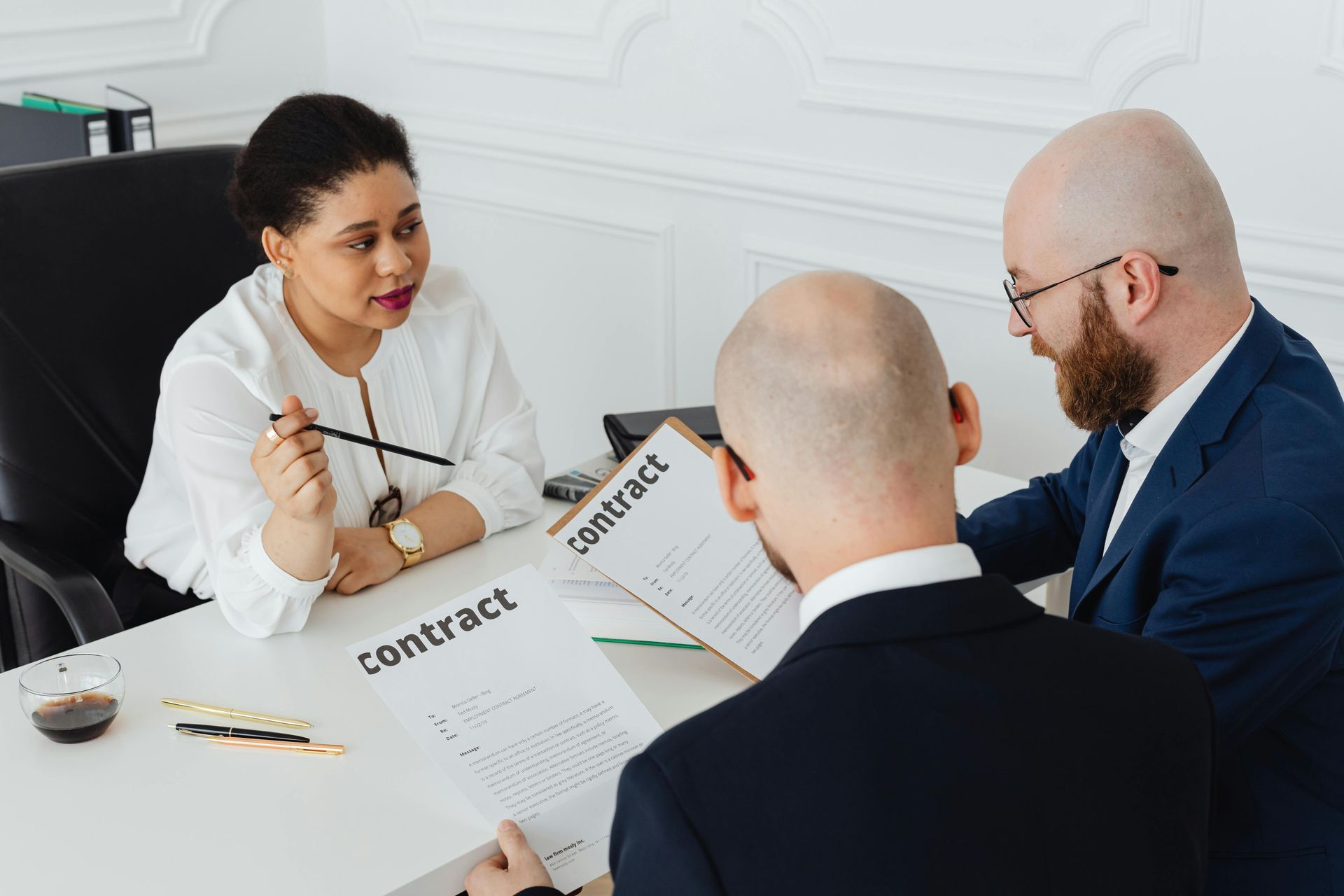 Three people in a meeting discussing contracts at a table in a bright office