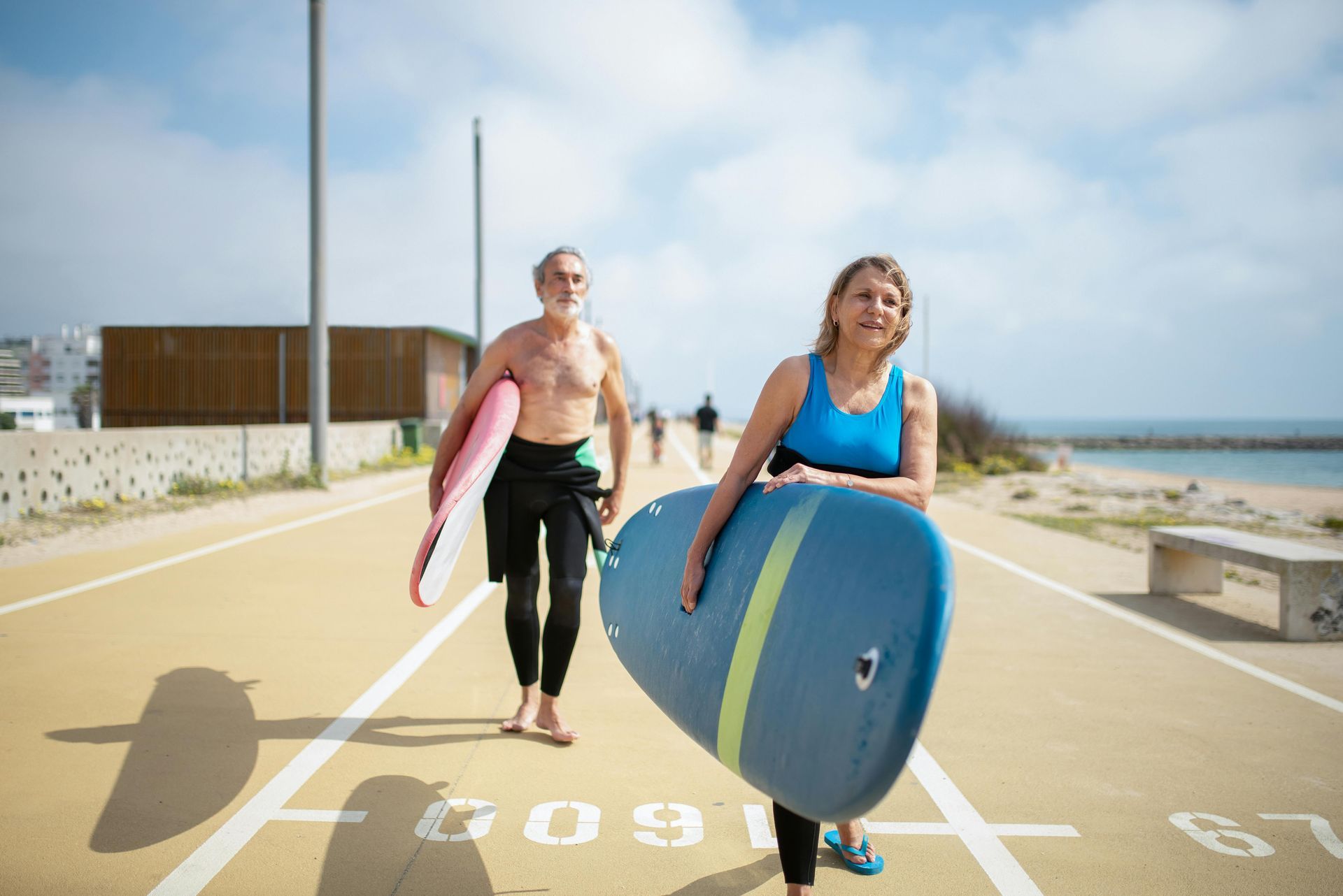 Two surfers carrying boards on a sunny beach path near the ocean